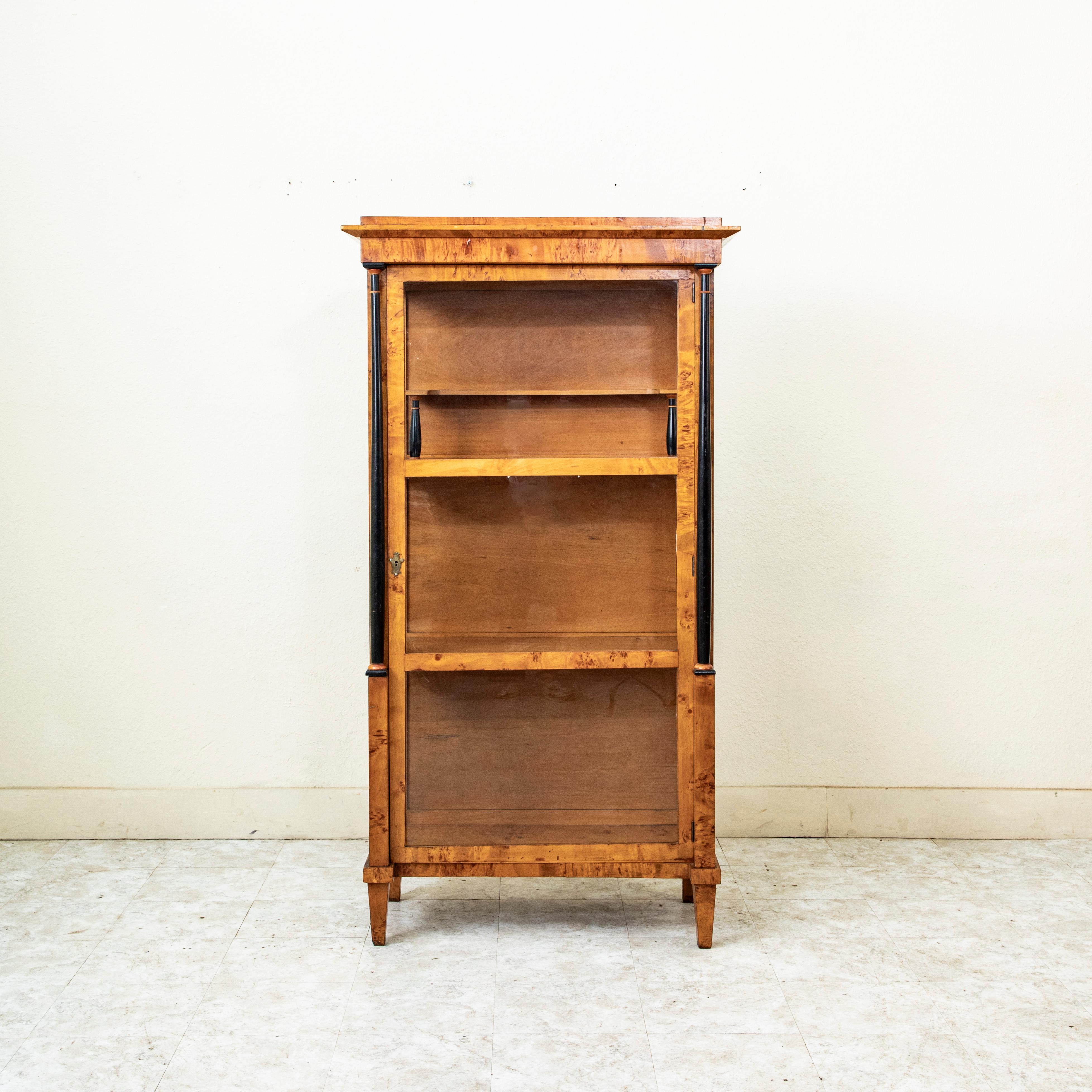 This early nineteenth century Biedermeier period Austrian vitrine is constructed of burled birch wood and features ebonized pearwood columns. Its single door and sides are fitted with its original hand blown glass. The door opens to allow access to