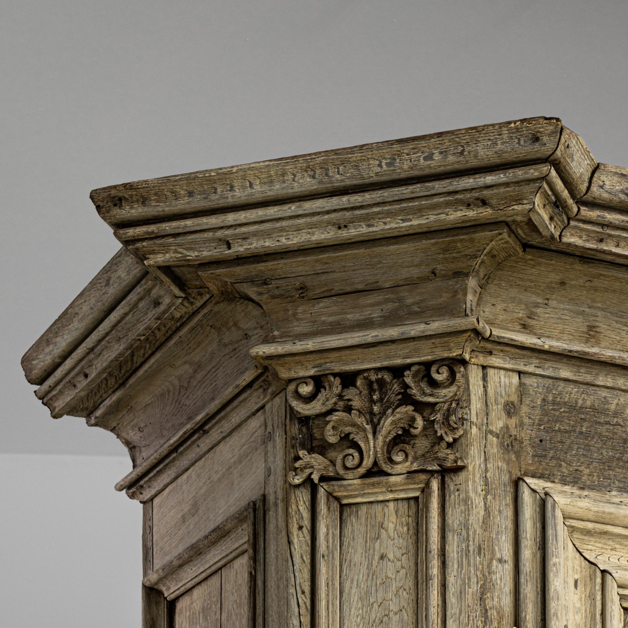 Regally poised like an ancient pillar, this armoire was made in Belgium circa 1800. Sturdily supported by its biomorphic feet, the vintage chest boasts a robust oak body with long panel doors decorated with sober neoclassical ornaments. Several