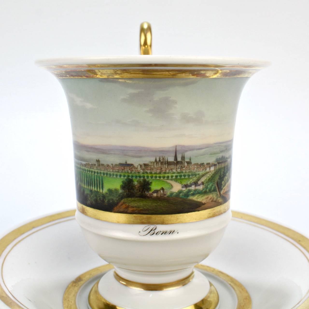 A fine antique German Biedermeier period topographical porcelain cup and saucer. 

The front decorated with a finely hand painted depiction of the city of Bonn. The reverse bears a dedication reading: 