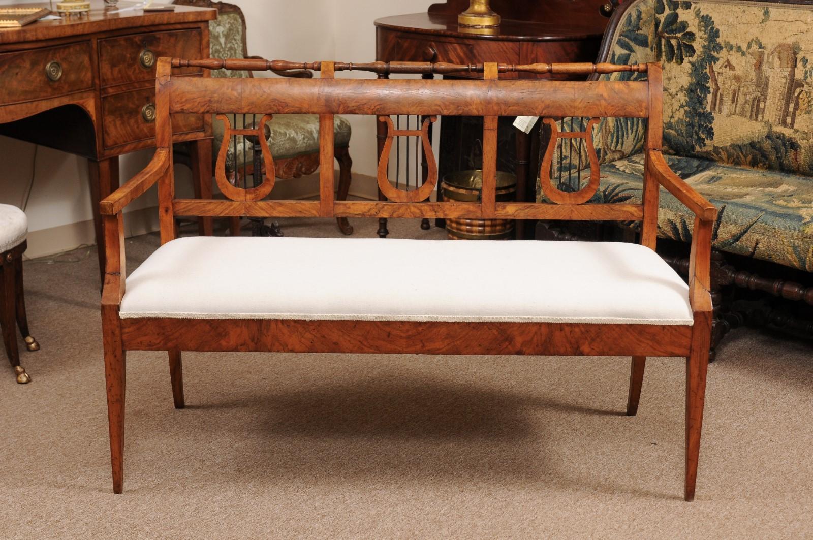 The Biedermeier settee with turned back railing with scroll above lyre back splat, upholstered linen seat below and terminating in tapered legs and splayed back legs.