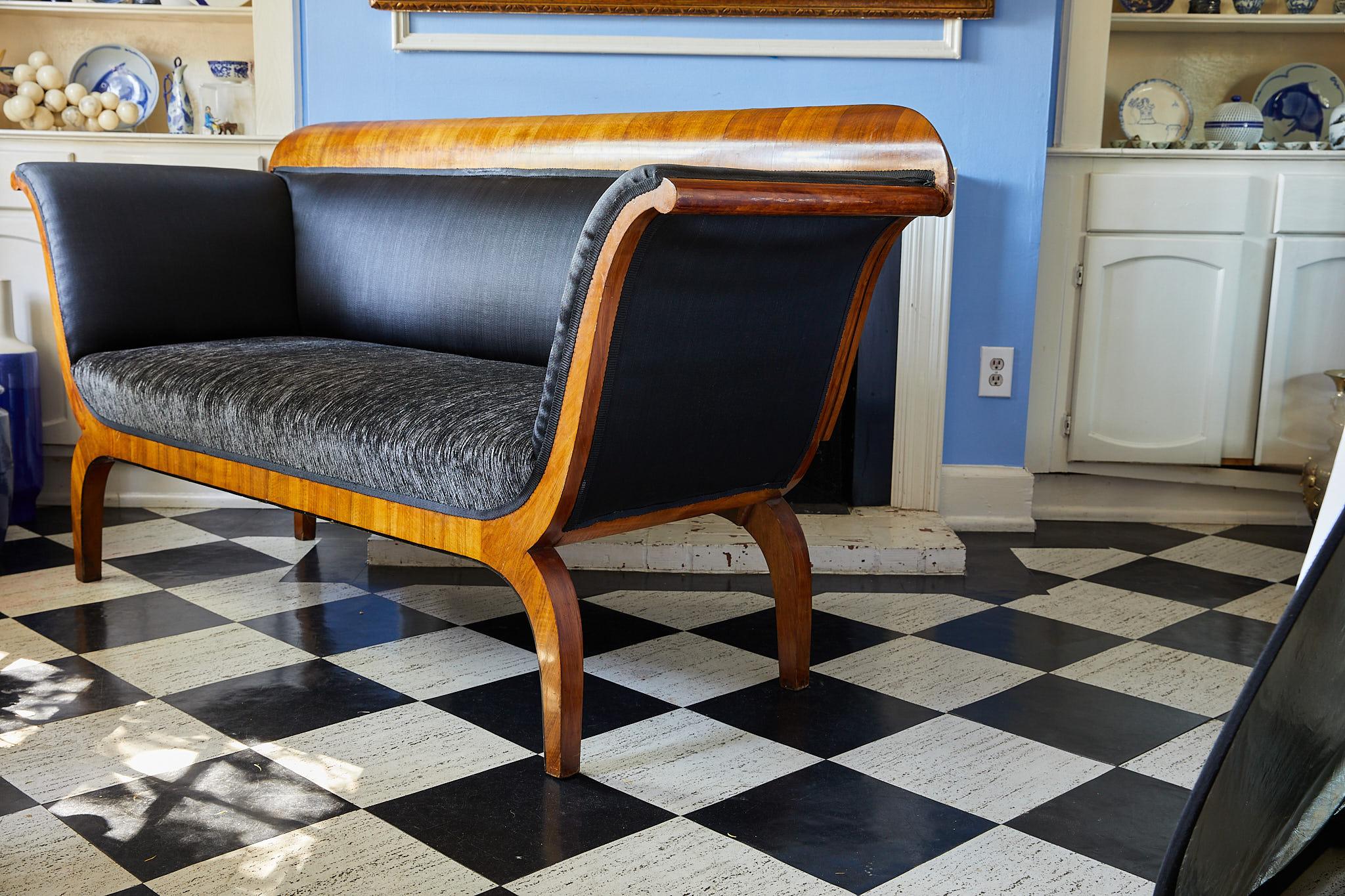 Early 19th century Biedermeier period sofa of elegant proportions. The sofa's crest rail, upswept arms, apron, and curved legs are veneered in Cherrywood. The arms and tight back of the sofa are upholstered in sleek black horsehair fabric while the