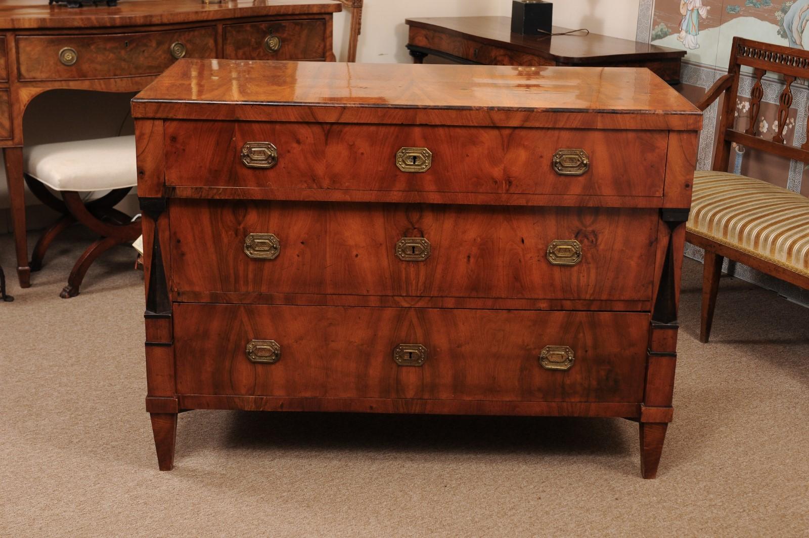 The early 19th century Biedermeier walnut commode featuring ebonized detail on the sides, 3 drawers with brass pulls terminating in tapered legs. 

 