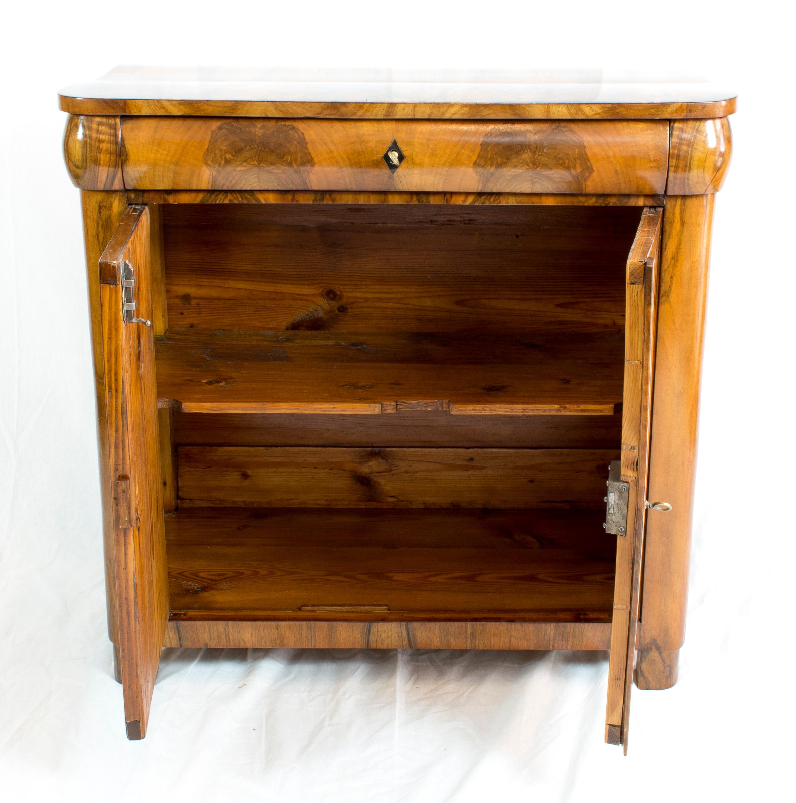 Beautiful Biedermeier half cabinet from the time of the Biedermeier, circa 1830. The furniture is covered with thick walnut veneer on a spruce body.
At the top there is a drawer, below are two doors. Extremely practical individual small piece of