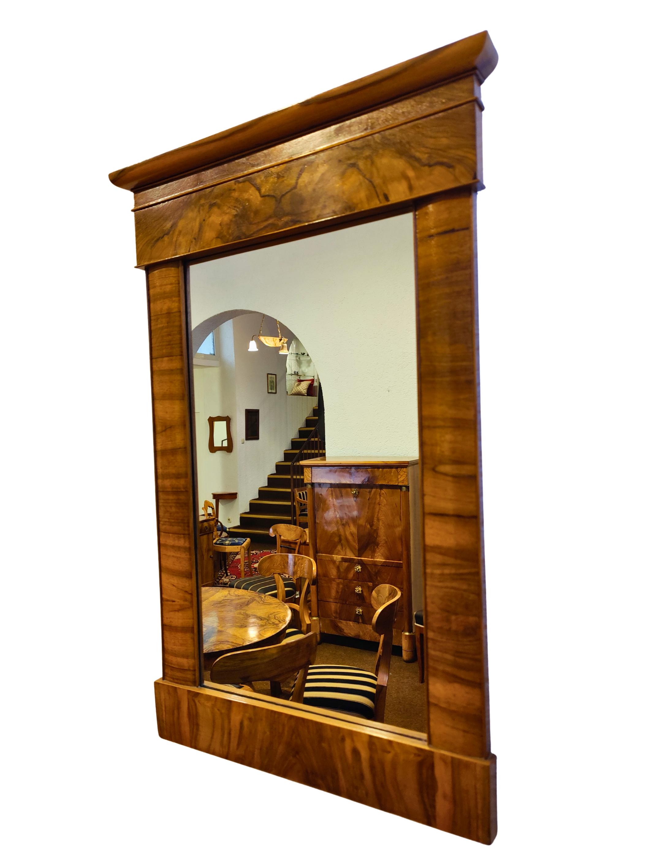 This elegant wall mirror dates from the German Biedermeier period around 1830 and is a fine example of early 19th century craftsmanship. The mirror is veneered in walnut over a softwood carcass and features a well-proportioned rectangular form with