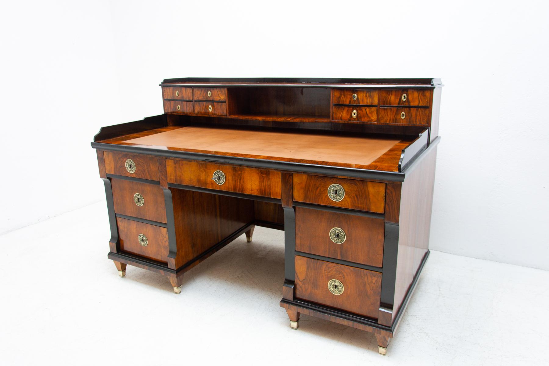 This Biedermeier writing desk was made in Austria-Hungary, circa 1830. It is made of walnut wood. The table is characterized by traditional elements of this style. Brass decorative elements are fitted on the door front. The table is in excellent