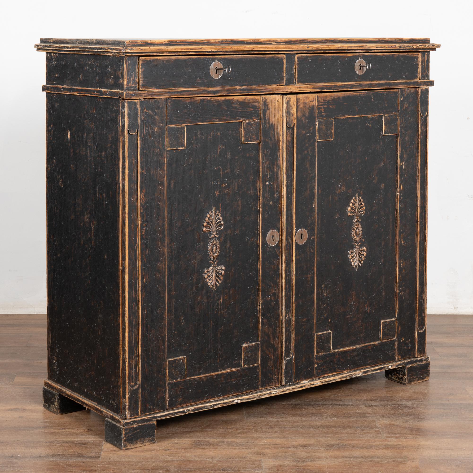 Black painted pine sideboard with clean lines and decorative applied carving to the two cabinet doors. 
The black painted exterior has been distressed revealing the natural pine below which adds to the warmth and character of this dramatic serving