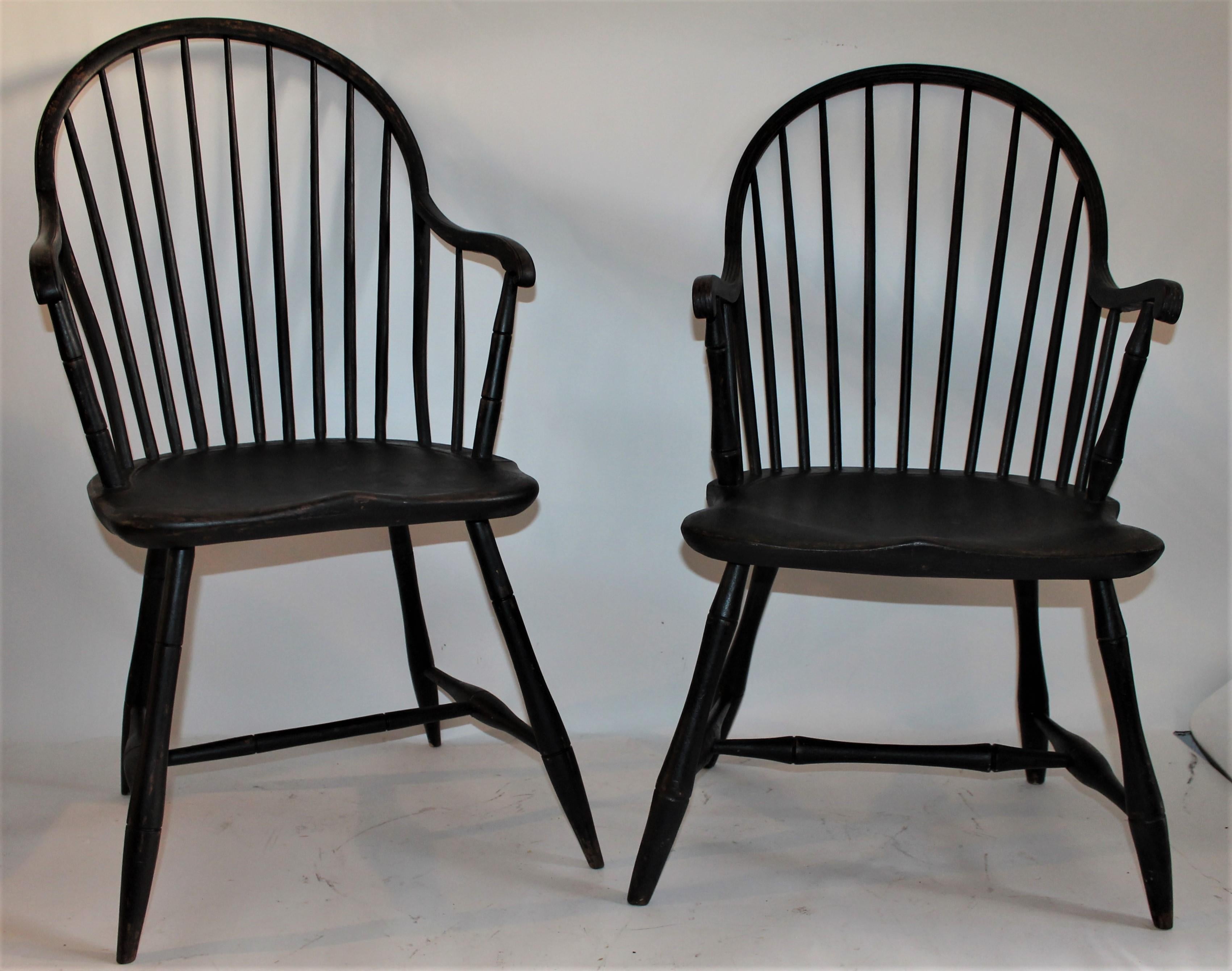 Early 19th century black painted Windsor armchairs in fantastic condition. They are not an exact match but very close. One has an antique repaired seat and the other does not. Note the curved arms on both New England chairs.