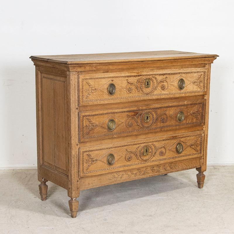 This classic French oak chest of drawers has been given new life with a bleached finish which has lightened the dark oak and brings out the lovely carved details of the paneled drawers, sides and feet. Carved wreathes encircle the central key hole