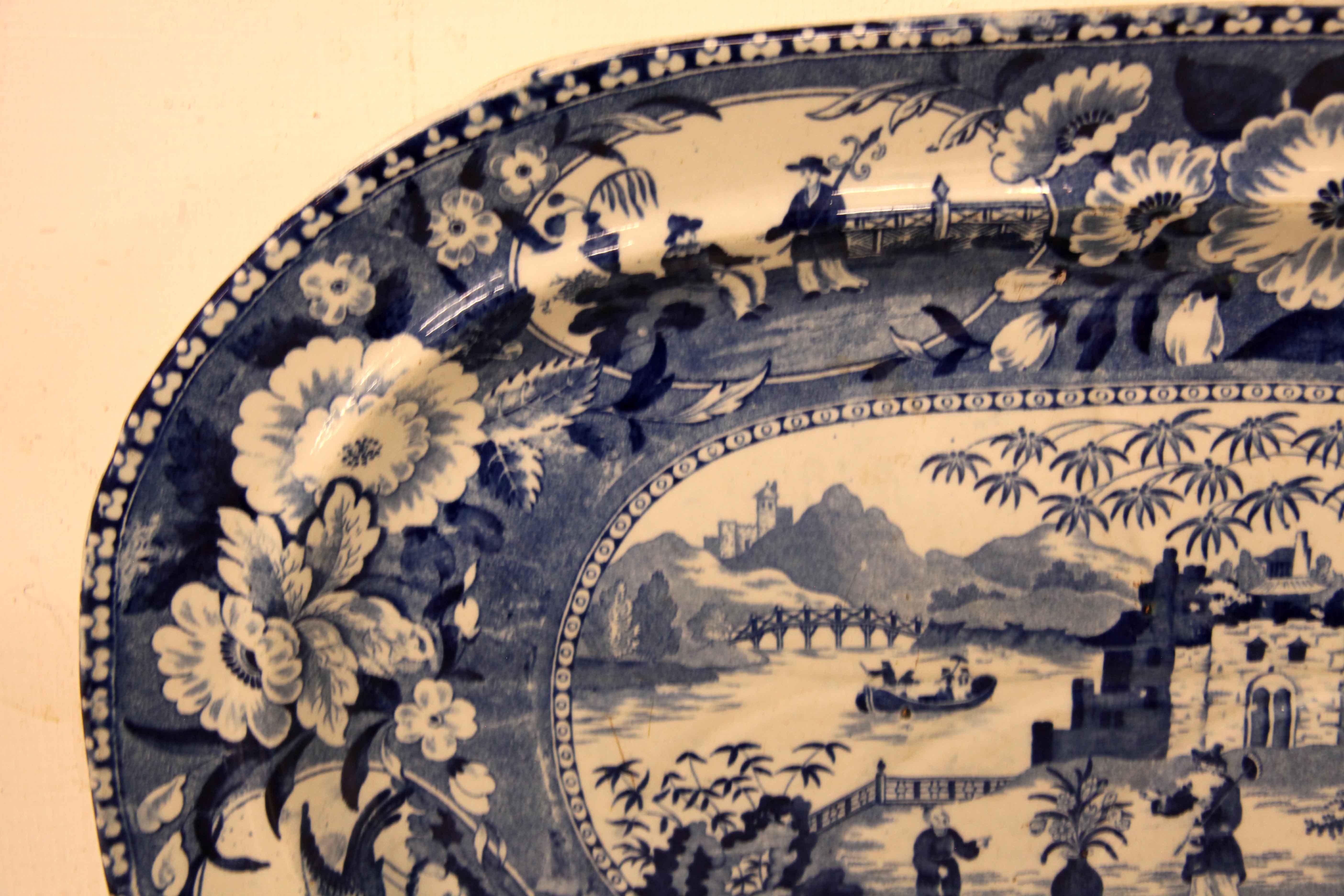 Early 19th century blue and white well and tree platter, the border has panels, one with oriental men with a fence and urn in the background, the other with two birds,  tree and bee; the panels are separated with large floral blooms and foliage. The