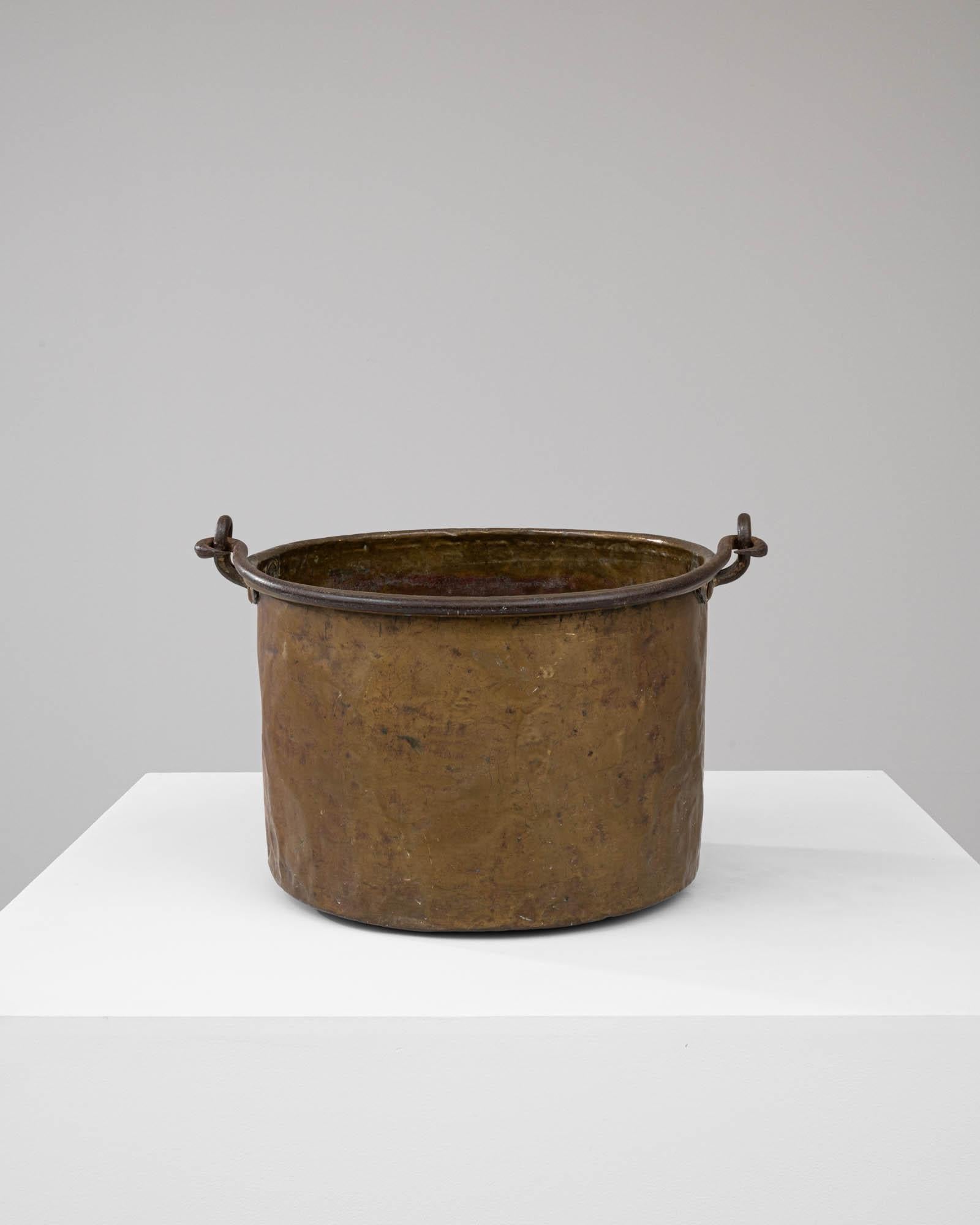 This early 19th Century Brass Bucket is a testament to enduring craftsmanship and utilitarian design. Once a staple in a bygone era, its solid brass construction bears a rich patina that tells tales of its service and longevity. The bucket features