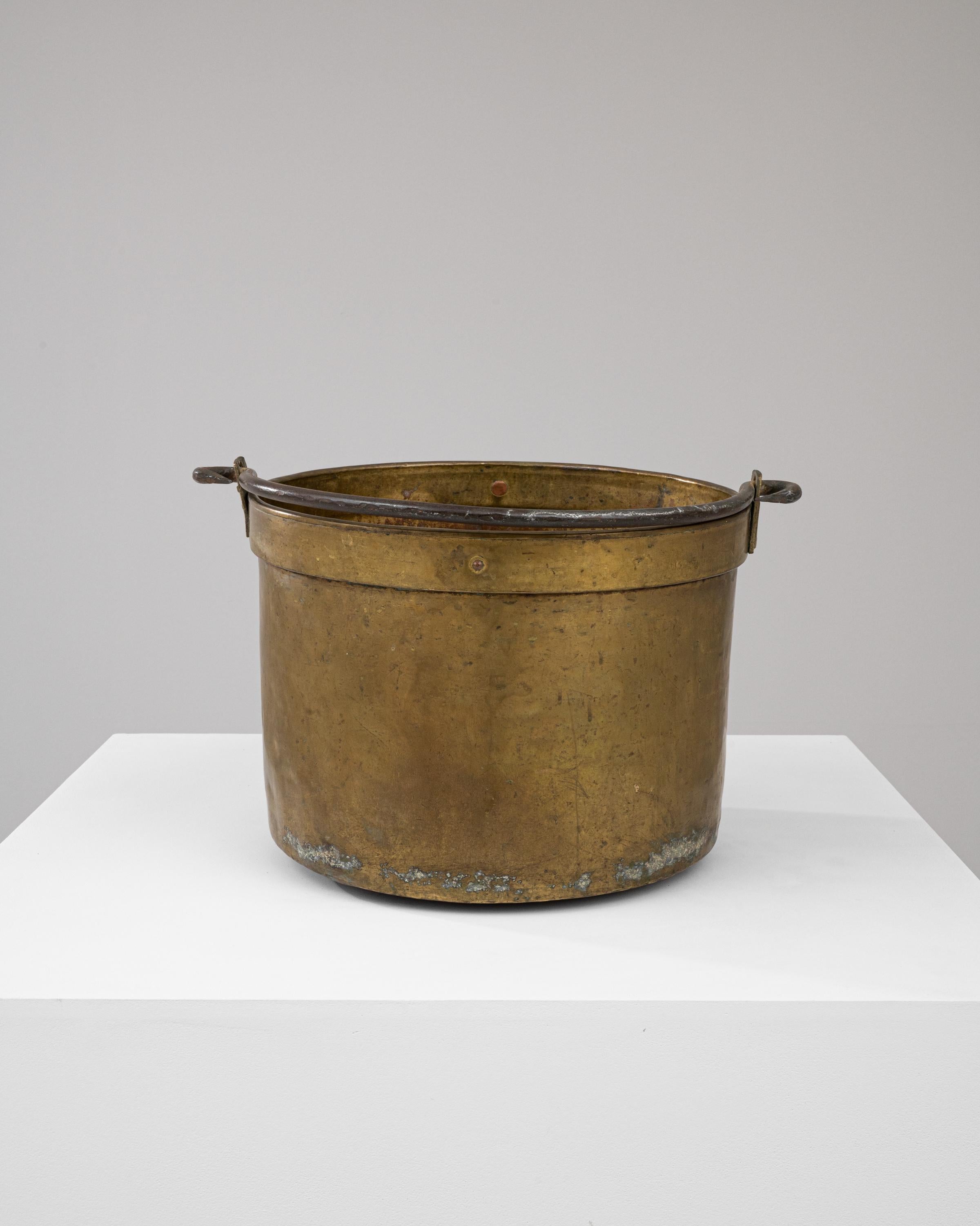 This early 19th Century Brass Bucket exudes a rich history and functional simplicity. Constructed from high-quality brass, its sturdy, cylindrical form is designed to endure the rigors of time. The surface showcases an exquisite patina that only