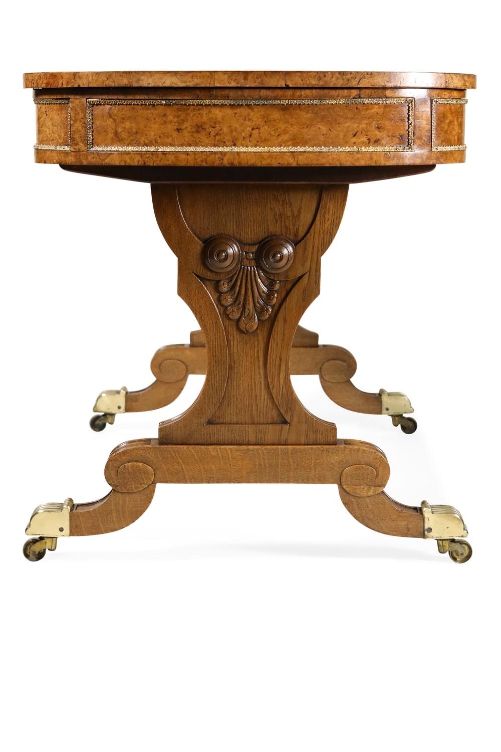 An unusual early 19th century brass-mounted pollard oak writing table, attributed to Gillows, the hinged rectangular leather-inset writing top with an adjustable writing slope on a ratchet flanked by semi-circular ends, the frieze with one long