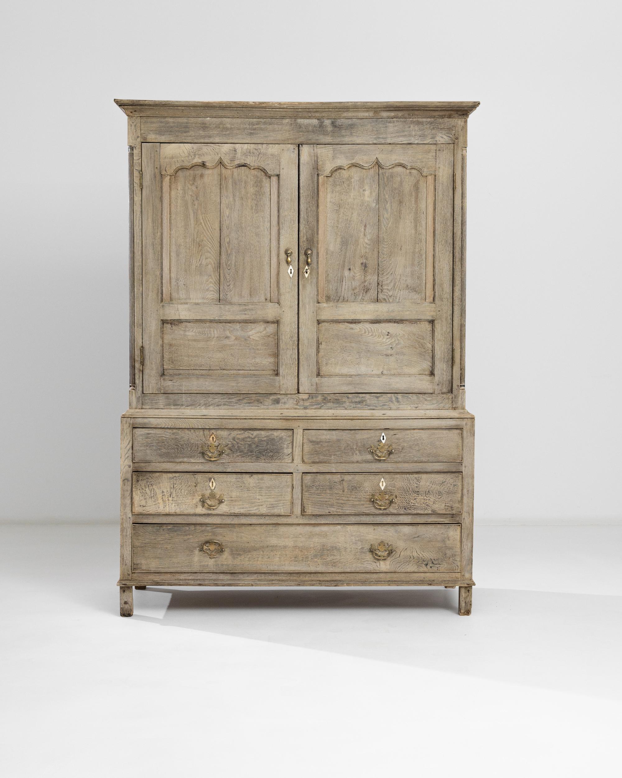 This robust oak cabinet was made in the UK circa 1800. Its deux-corps anatomy provides a spacious upper compartment with two raised doors decorated with boldly carved arches and a lower section with five drawers. The presence of the pale finish is