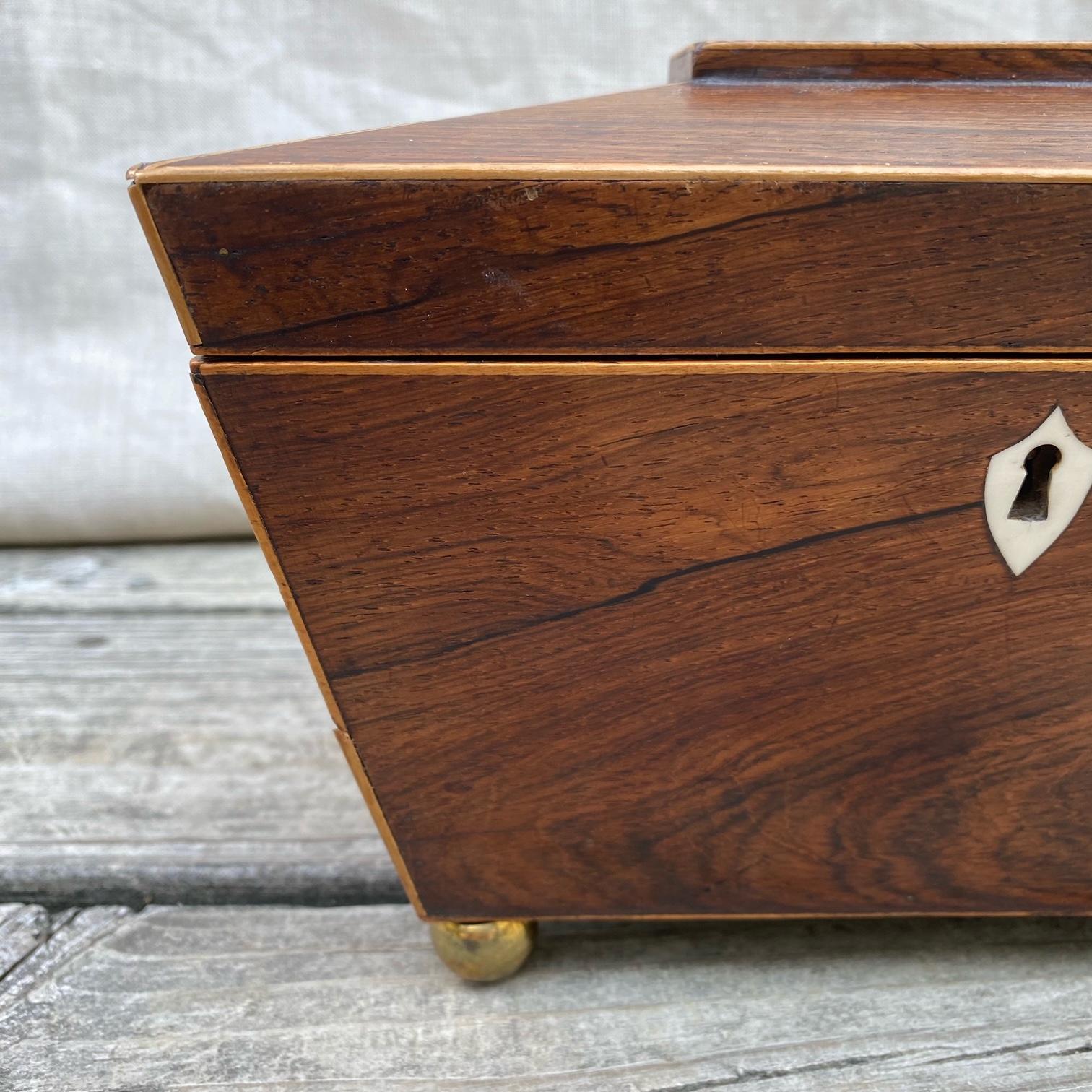All original early 19th century English Georgian inlaid tea caddy in sarcophagus form. The body has a hinged lid with original red top, beautiful escutcheon, knobs and bun feet. Original condition, with both inlaid lidded compartments intact.