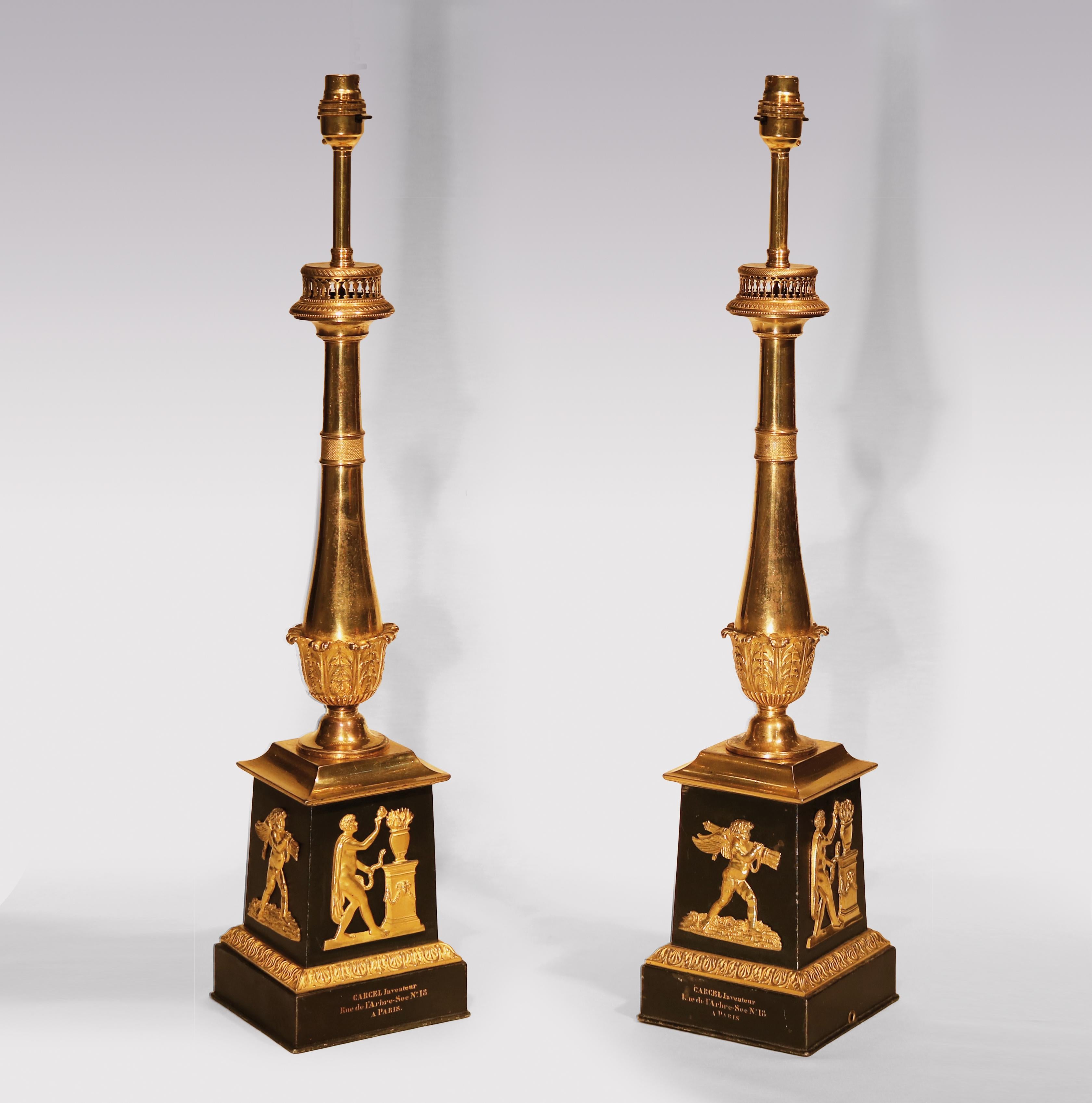 A pair of early 19th century carcel oil lamps, having engine turned stems with acanthus leaf decoration raised on square bases with applied classical mounts ending on plinth bases stamped:
