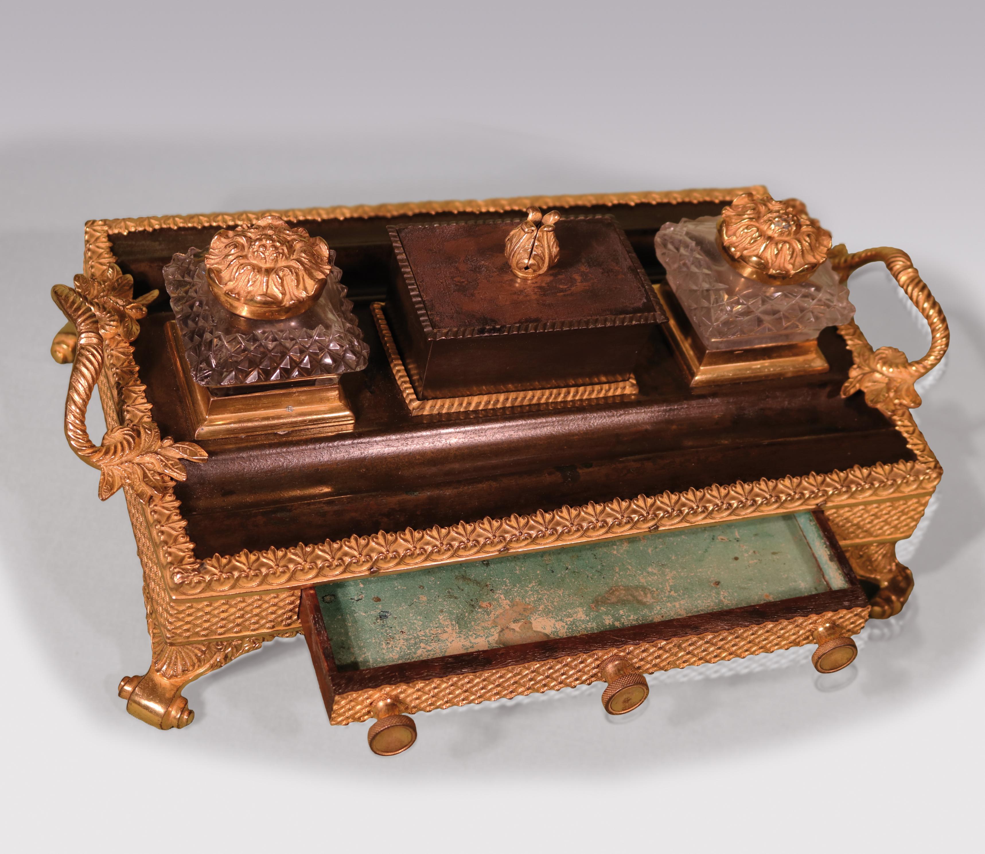 An early 19th century Regency period bronze and ormolu Pentray with cut glass inkwells, having leaf & scroll handles above fret decorated frieze with central drawer, supported on shell scroll feet.