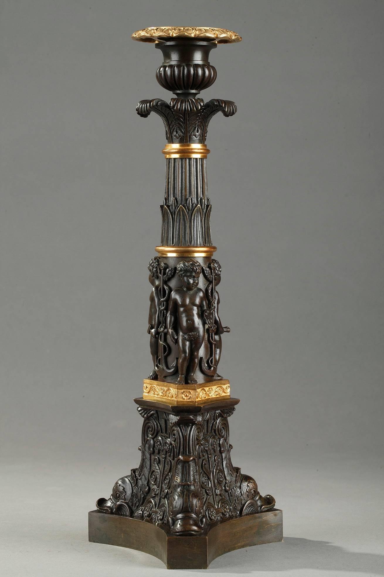 Large 19th century restauration candlesticks in ormolu and patinated bronze. The barrel is divided into three registers separated by gilt bronze rings. The pair features young cupids symbolizing the arts (painting, music and sculpture). The upper