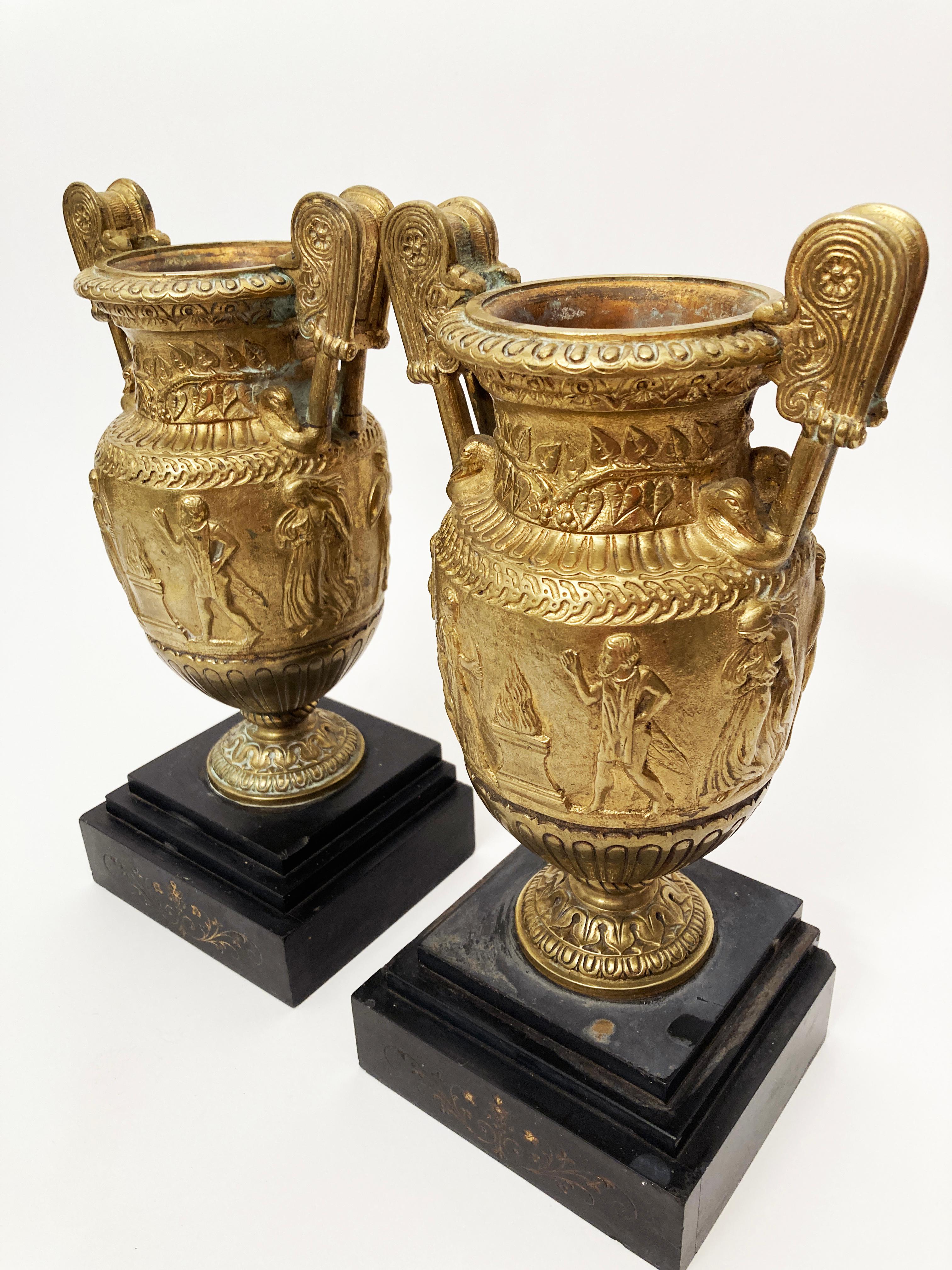 This pair of early 19th century Grand Tour Period bronze gilt volute krater urns on stone bases are absolutely breathtaking. The base is a heavy black slate with etched Neo-classic floral motifs on the front of each base. The metal is stunning with