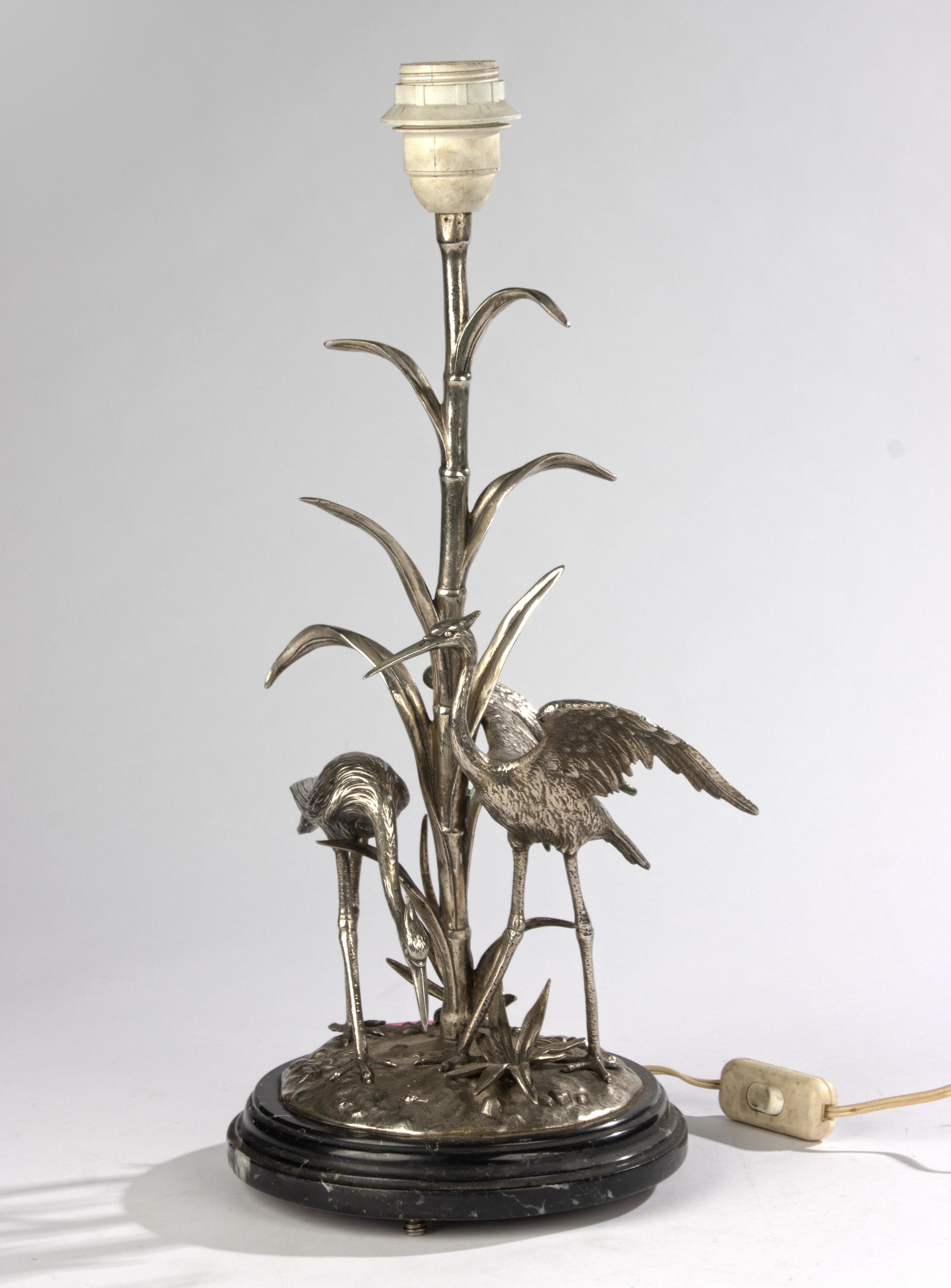 
Una hermosa lámpara de mesa antigua, con una estatua de bronce de dos garzas en los juncos. La lámpara se alza sobre una base de mármol negro, y la base de mármol tiene unas pequeñas y gráciles patas, de modo que el cable eléctrico queda bien