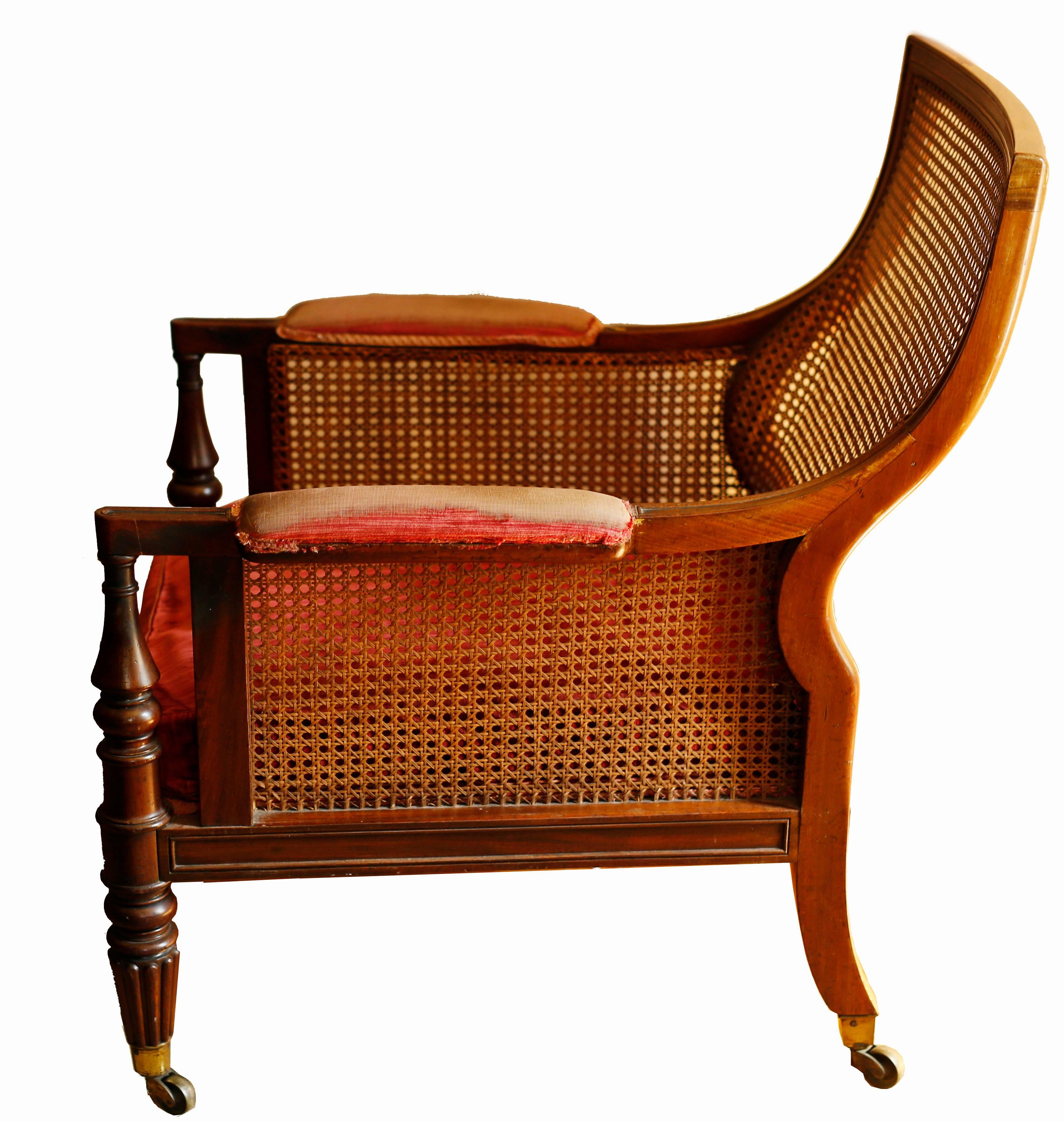 A handsome regency library bergere after the French antique manner, this mahogany chair features a Grecian-scrolled caned back and a generously proportioned seat.  This chair is nearly identical to a pair supplied to the Library at Mere Hall