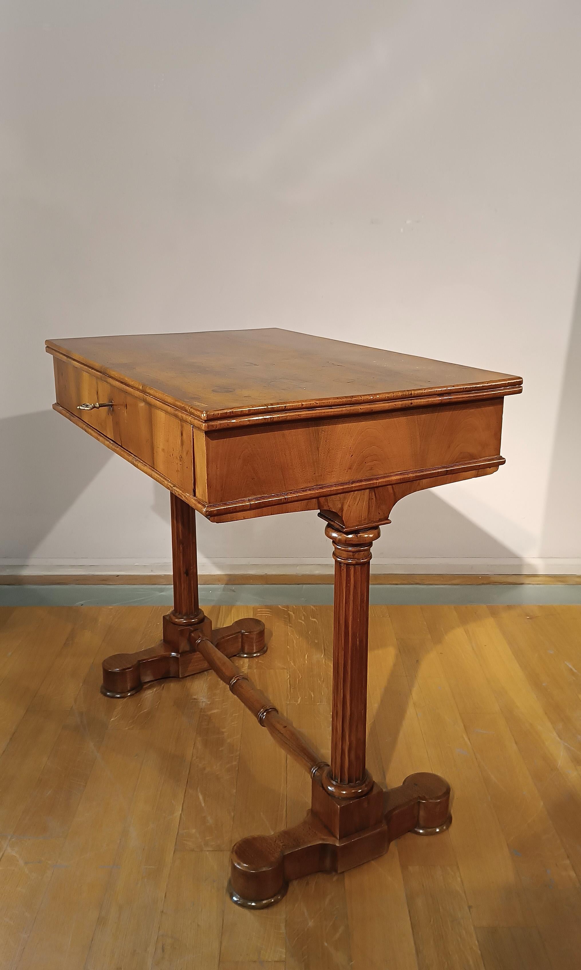 Elégante table basse en noyer blond sculpté. Conçue à l'origine comme table de travail, elle peut être utilisée comme petit bureau ou console. Les colonnes cannelées et le repose-pieds moulé lui confèrent une touche de classe, tandis que le plateau