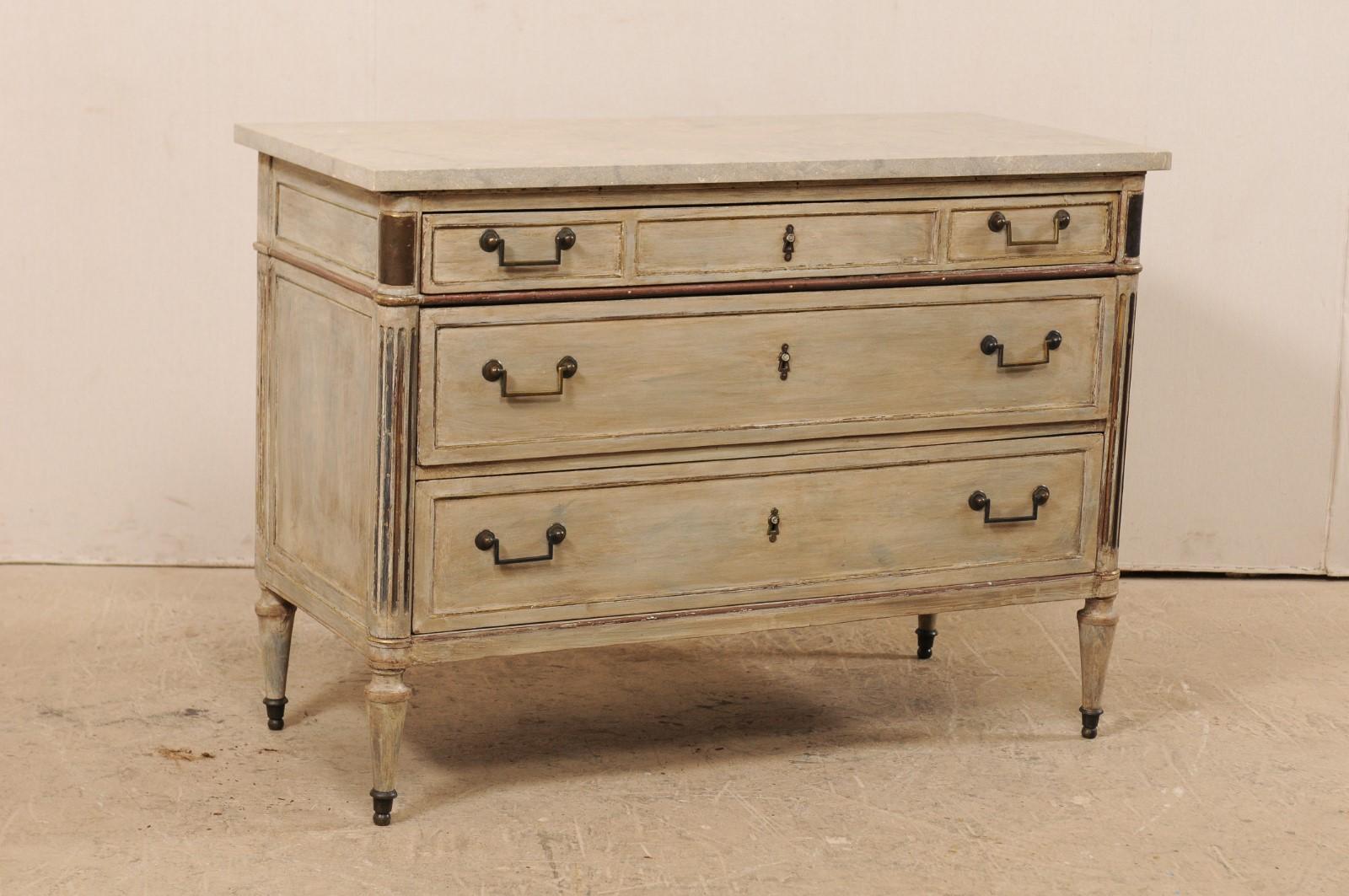 A French early 19th century wood carved chest of drawers with stone top. This antique chest from France features a rectangular-shaped fossilized limestone top, with rests atop a neoclassical case with rounded side posts which are fluted and