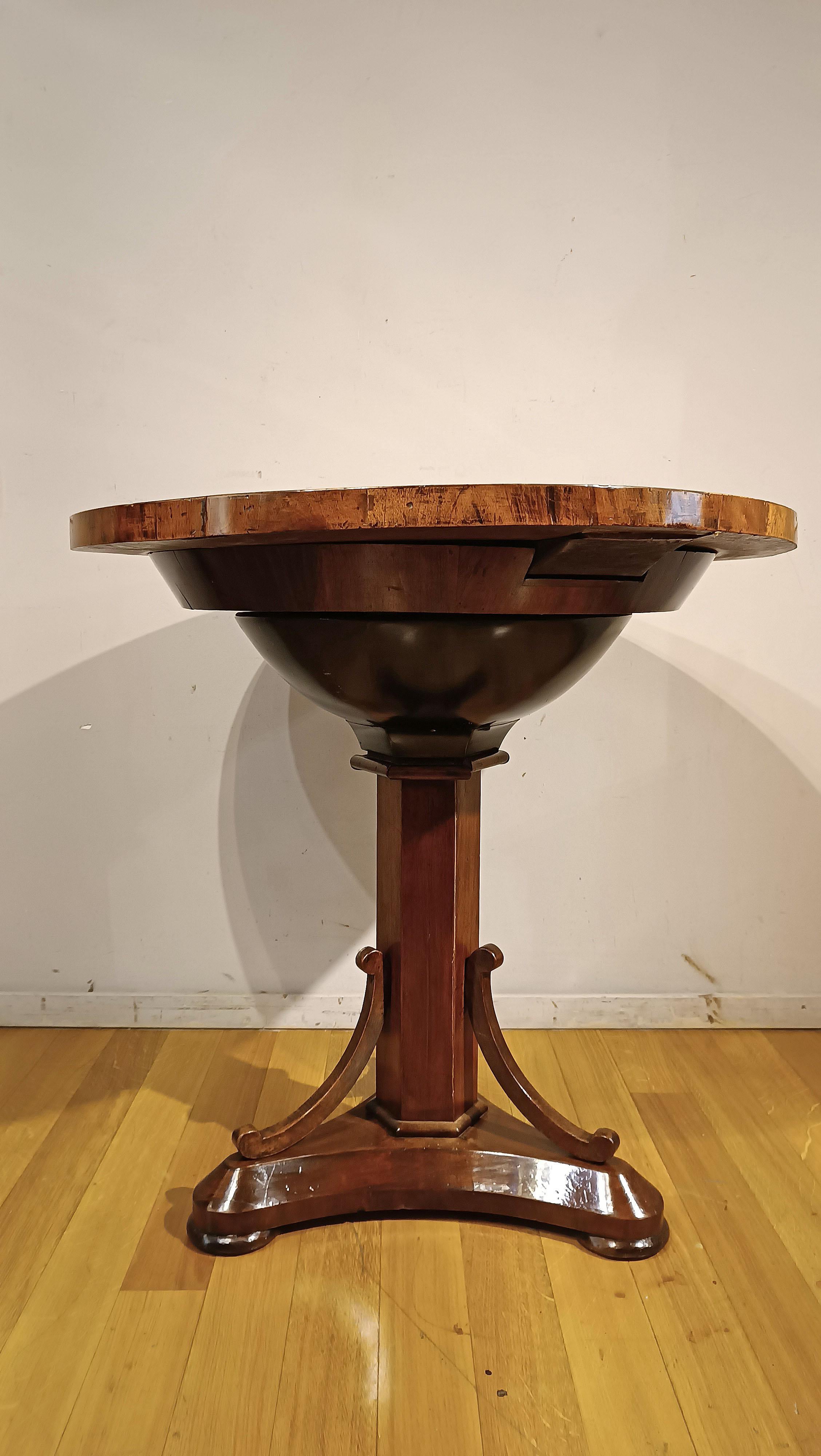 Elégante table basse en noyer massif avec placage de racine de noyer, présentant un plateau rond soutenu par une tige centrale hexagonale, qui se termine par trois pieds avec une base unique ornée de charmantes boucles décoratives. Cette pièce