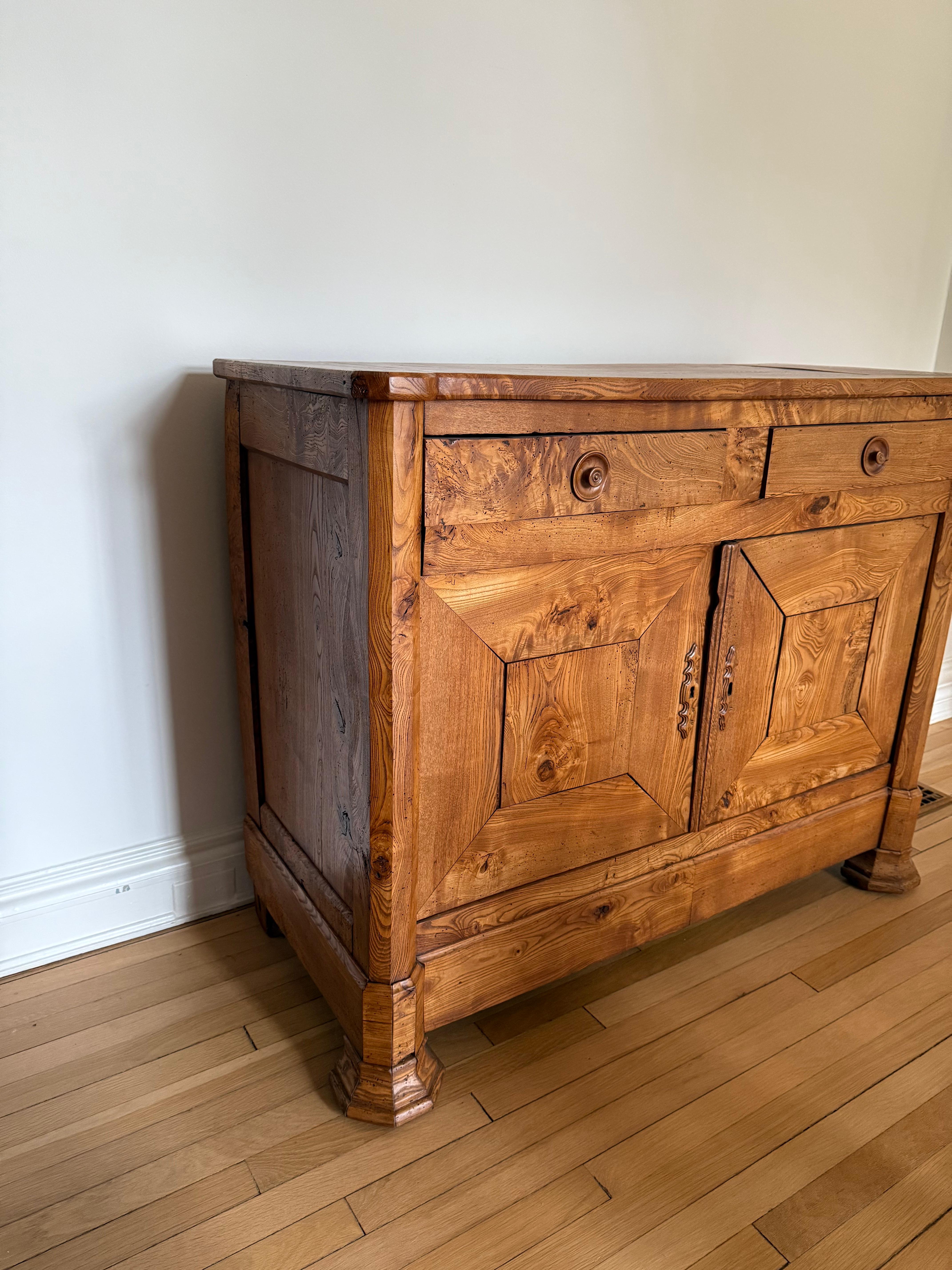 An outstanding and exceptionally rare early nineteenth-century burr elm buffet, notable for its rich colour, striking grain pattern, and elegant proportions. This refined piece features two short drawers above a pair of panelled cupboard doors, all