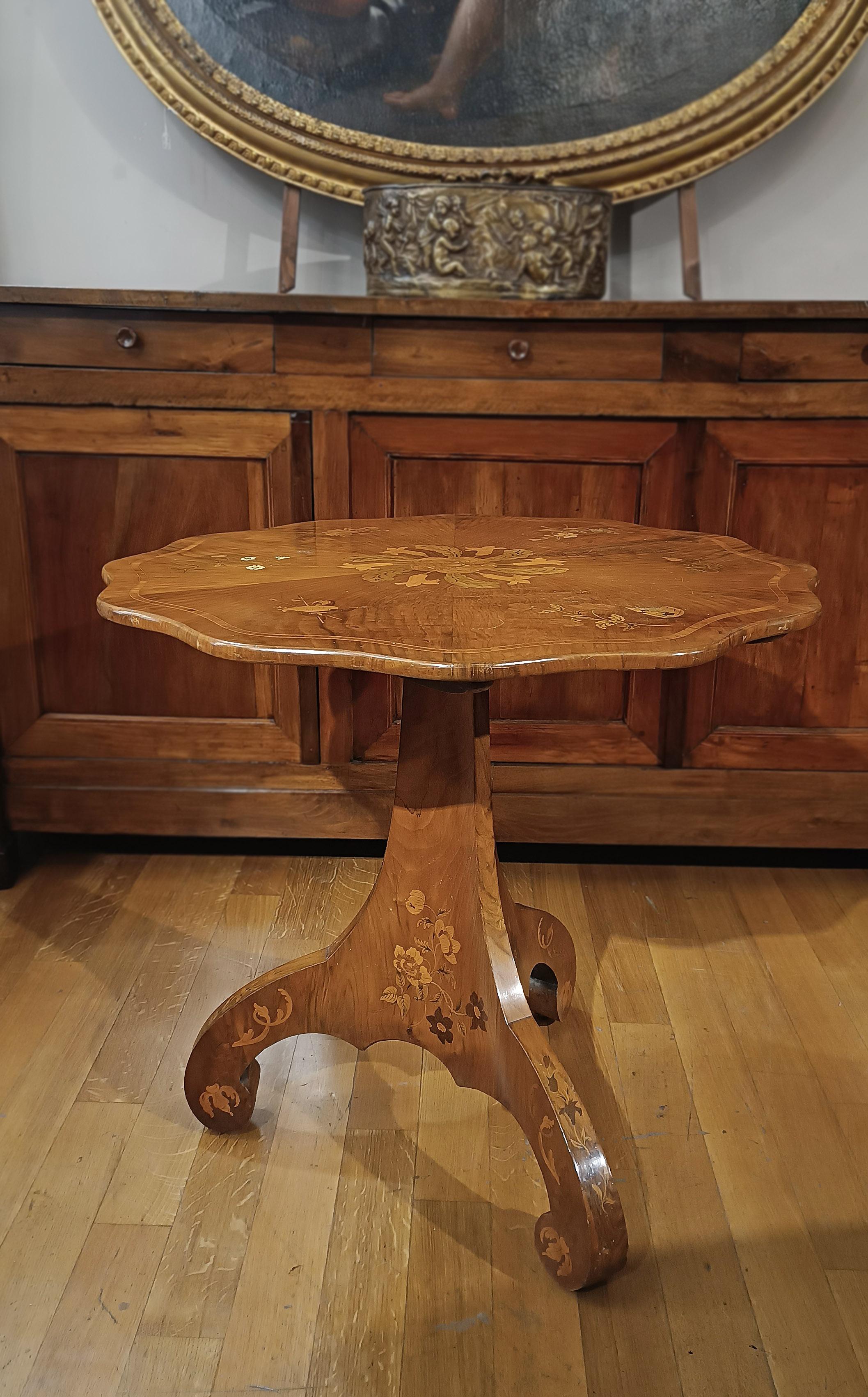 Elegant walnut “sail” small table, enriched with refined fruitwood inlays. The decorative inlays, which stand out for their great elegance, adorn the top, legs and shaft of the table with plant motifs. On the top, delicate coats of arms, flowers and