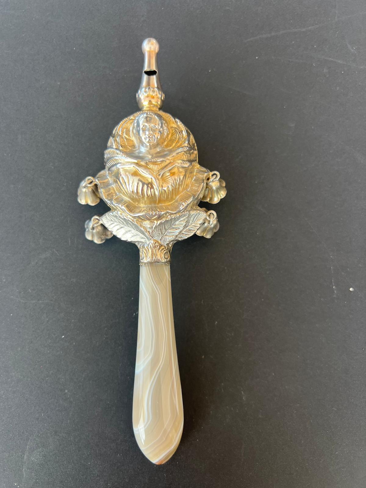 Rare chased silver rattle with whistle from the early 19th Century. The rattle depicts a face of a child surrounded by petals and leaves. It may also be a cabbage. There are four small lily of the valley flowers around the rattle as doorbell. The