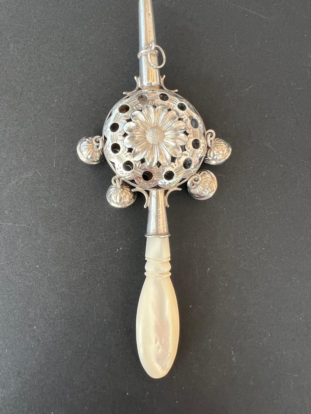 Rare chased silver rattle with whistle from the early 19th Century. The rattle depicts a flower. There are four small lily of the valley flowers around the rattle as doorbell. The handle of the object is certainly made out of mother of pearl. On the