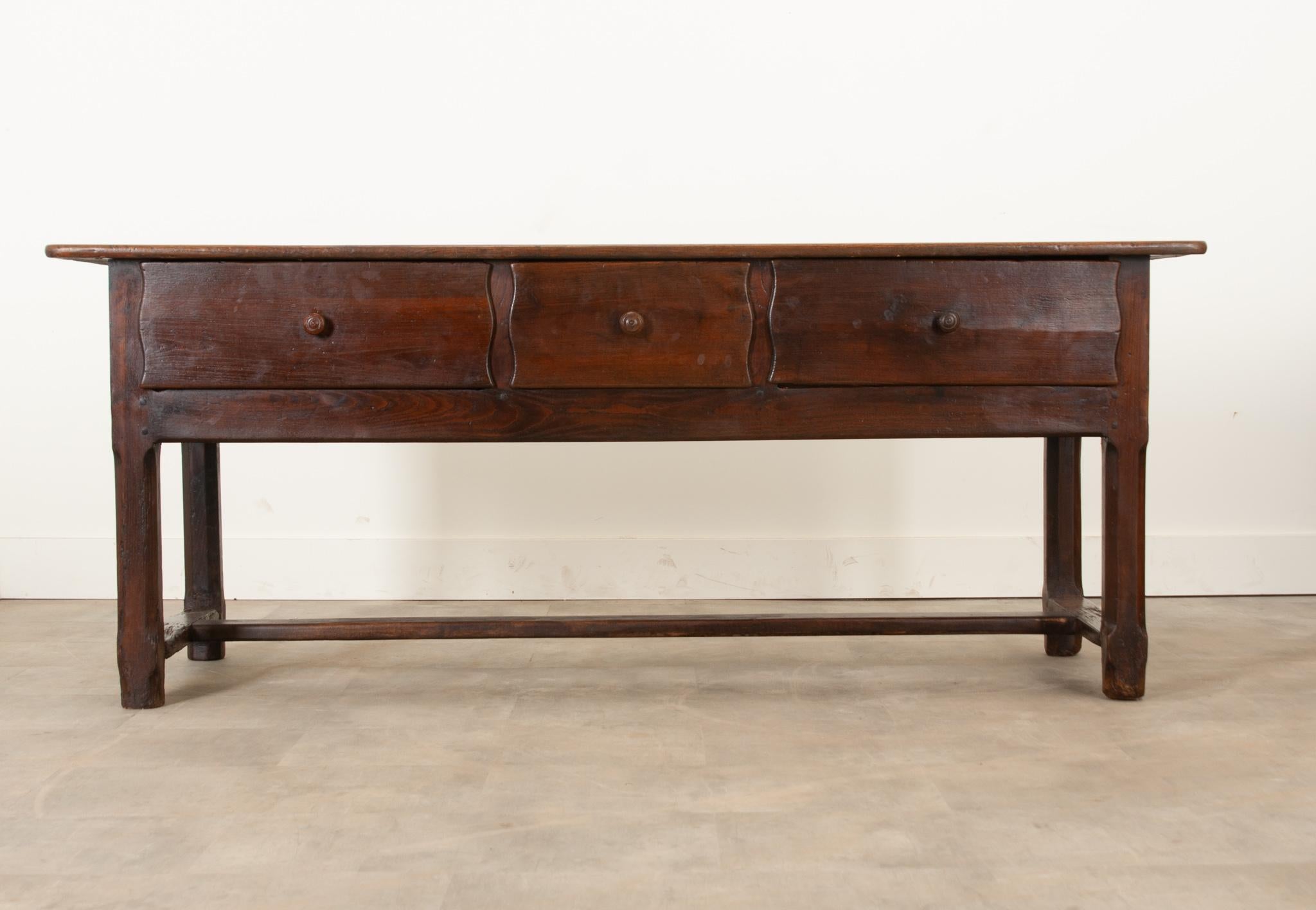 Crafted circa 1800 in England, this handsome server is the perfect provincial touch to any space. The solid chestnut has gained a fantastic patina. The top showcases the distinctive wood grain beautifully. Three drawers with scalloped edges are