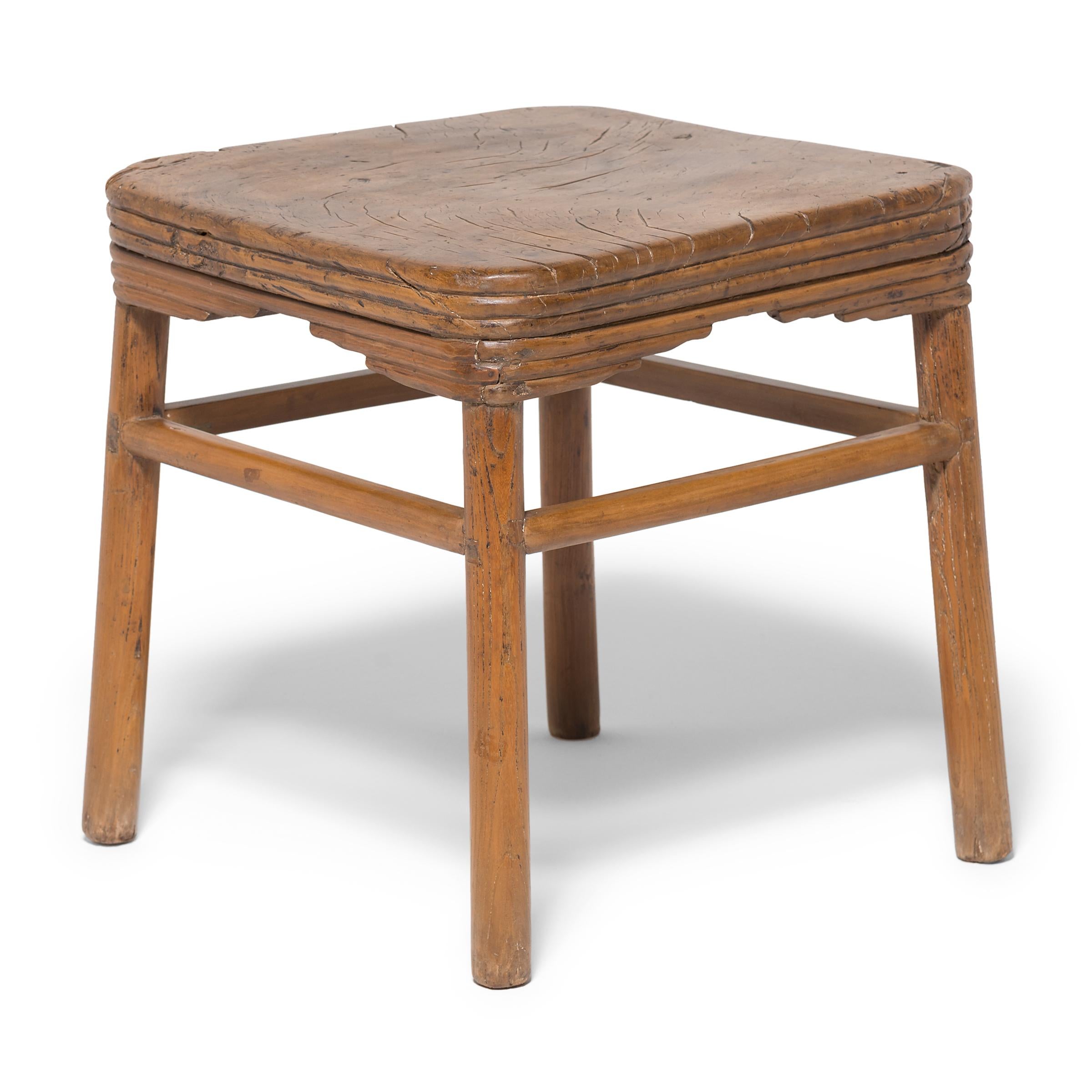 This early 19th century Chinese stool features a burled linden top with a richly swirled grain. A single burl of linden was hand-carved to create the stacked design of the sides and seat. The stool has round splayed legs and a texture that calls to