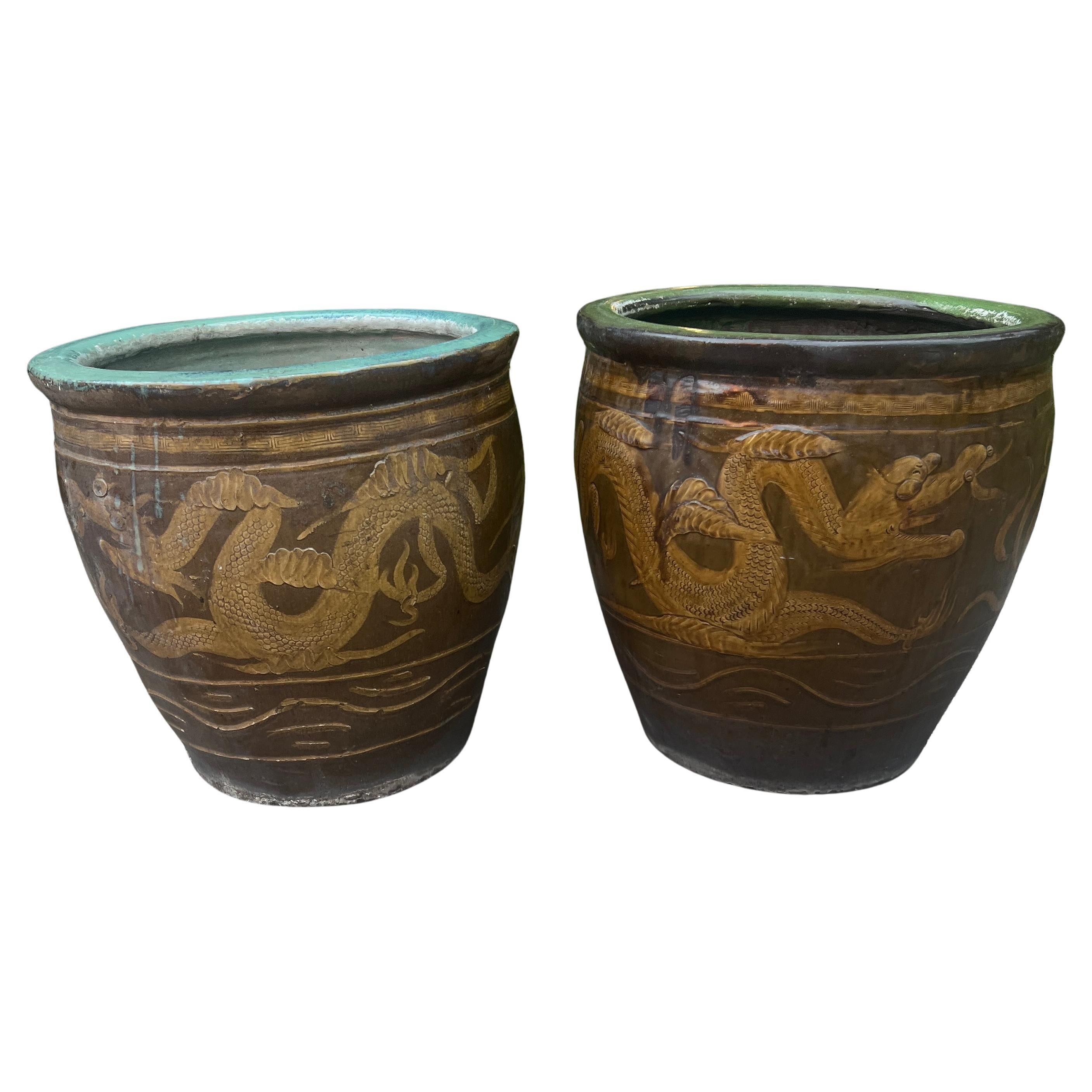 Paire de jardinières chinoises en grès émaillé du sud de la Chine. Les pots sont ornés d'un dragon traditionnel qui s'enroule autour du corps et qui poursuit la perle éternelle enflammée. Le dragon, qui représente la chance, est sculpté dans