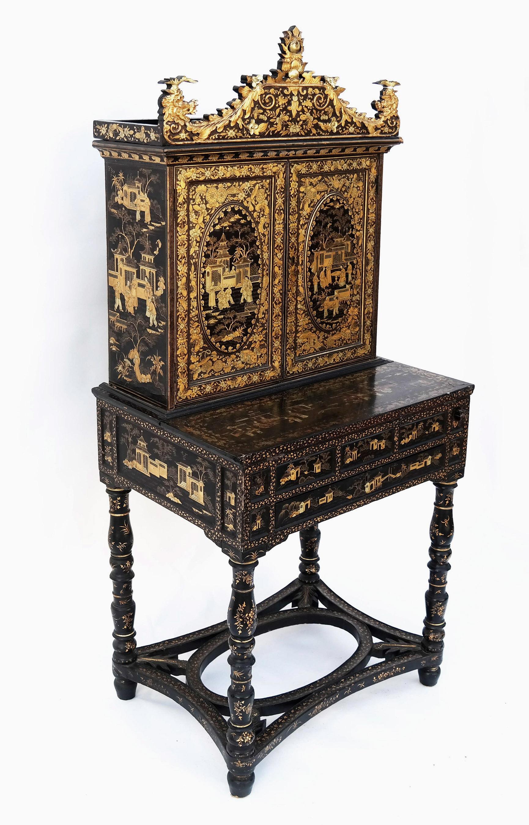 An exceptional black lacquer and silver and gold gilt decorated bonheur du jour from the early 19th century. The upper case is surmounted by a carved pediment with dragon finials and foliate designs. Two doors with painted oval panels depict village