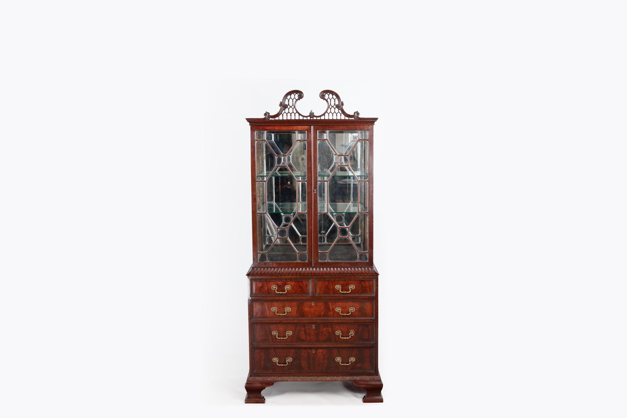 Early 19th Century two-door Chippendale display case in the Chinese style. The finely carved swan neck pediment with open fretwork design sits above two astragal glazed doors that open to reveal a mirror-backed interior. To the lower section, with