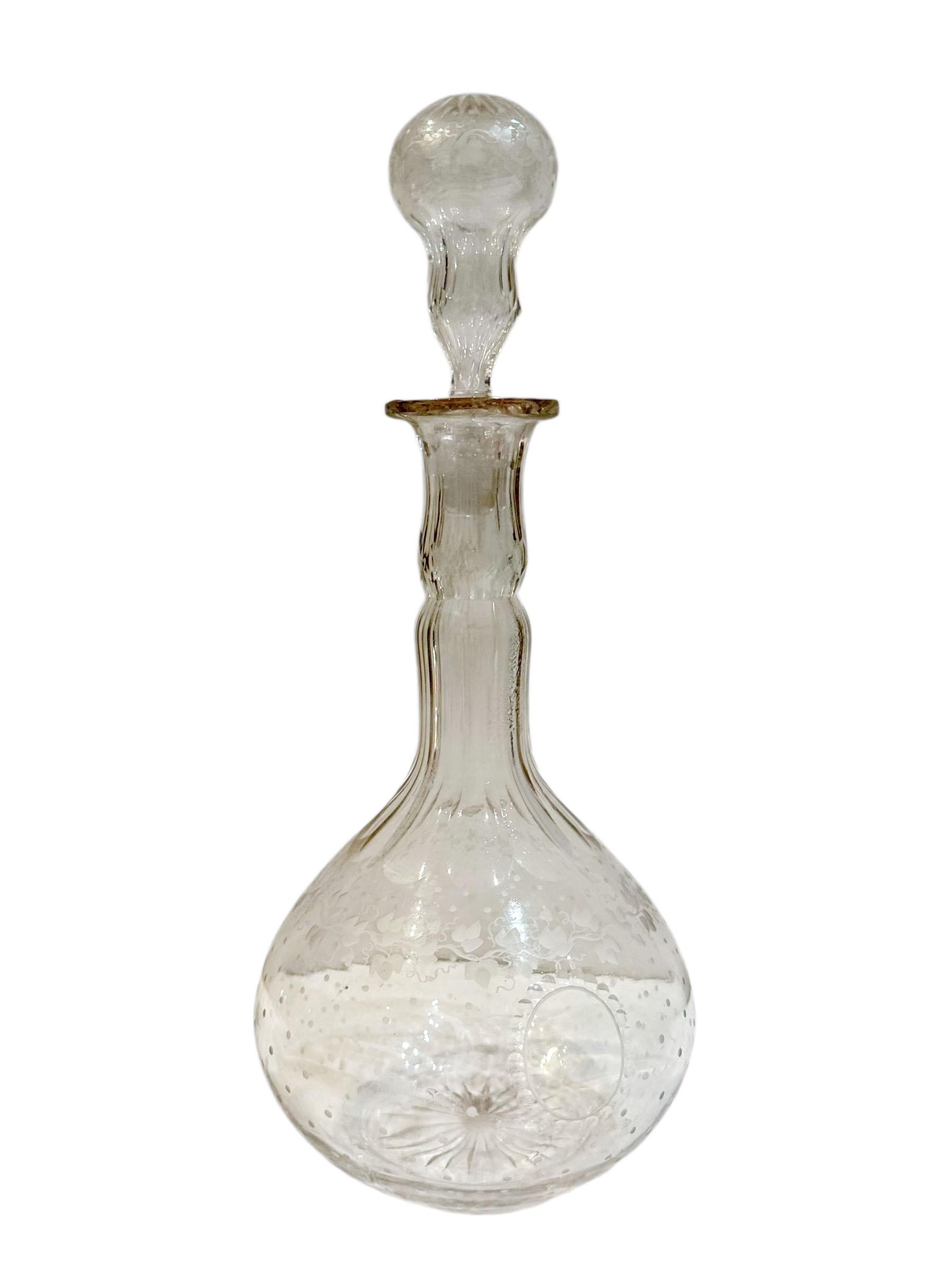 Elegante botella de vidrio continental de principios del siglo XIX, totalmente artesanal y con bellos detalles. El cuerpo está decorado con delicados motivos grabados de hojas y lunares, que muestran el fino arte de la época. Presenta un tapón alto
