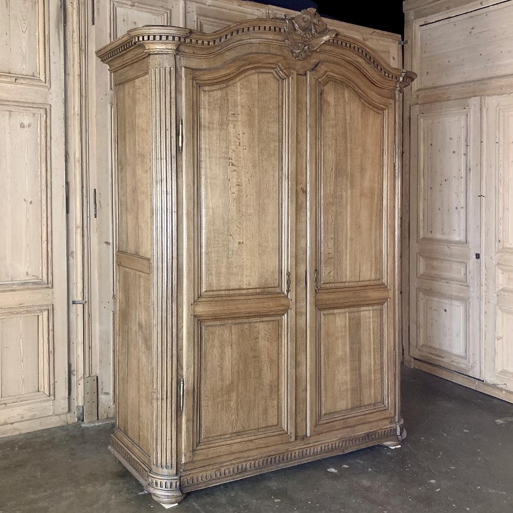 Early 19th century country French stripped oak armoire is a masterpiece of rural artisanry, designed with architecture rooted in ancient Greek and Roman classicism. The bold chapeau de gendarme cornice is centered with a heraldic crest, and the