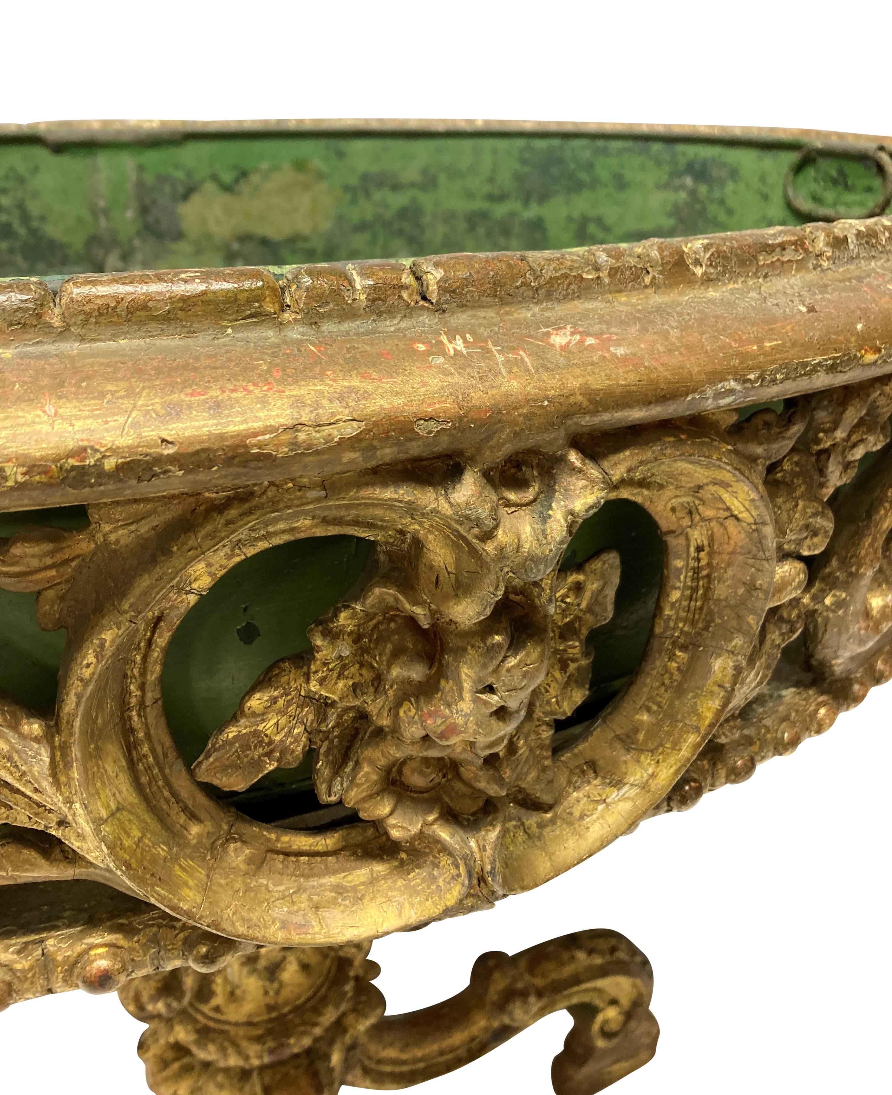 A French Louis XV style country house giltwood jardiniere of oval form. The water gilded base, which has a good 'dry' patina, is intricately carved. There are some historic loses, and one foot has been built up. It has a green painted tin liner.