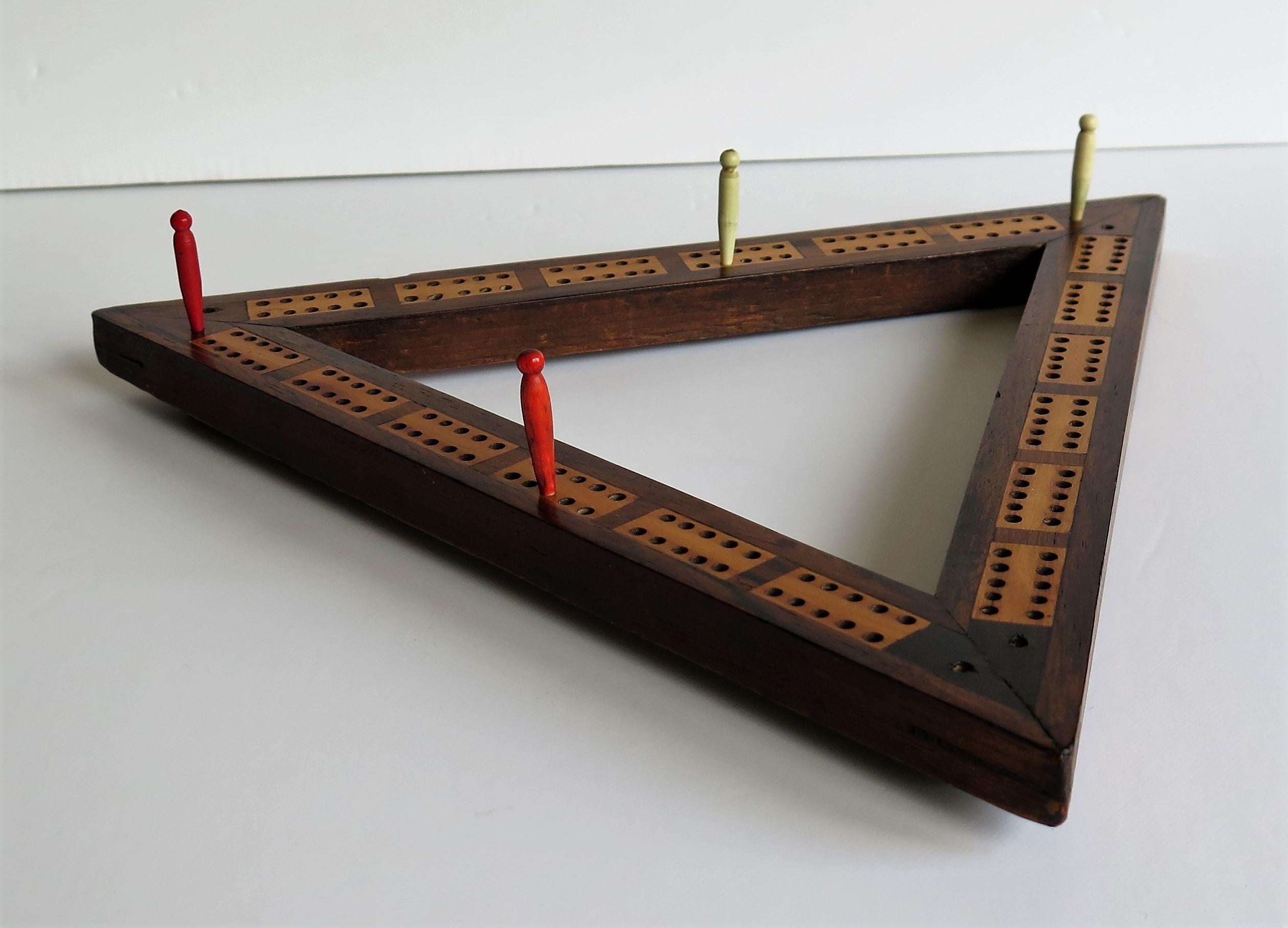 This is a late Georgian early 19th century, triangular shaped Cribbage game score board made of various inlaid woods and complete with four bone pegs.

This board is very well handmade with a triangular jointed frame which has been carefully inlaid