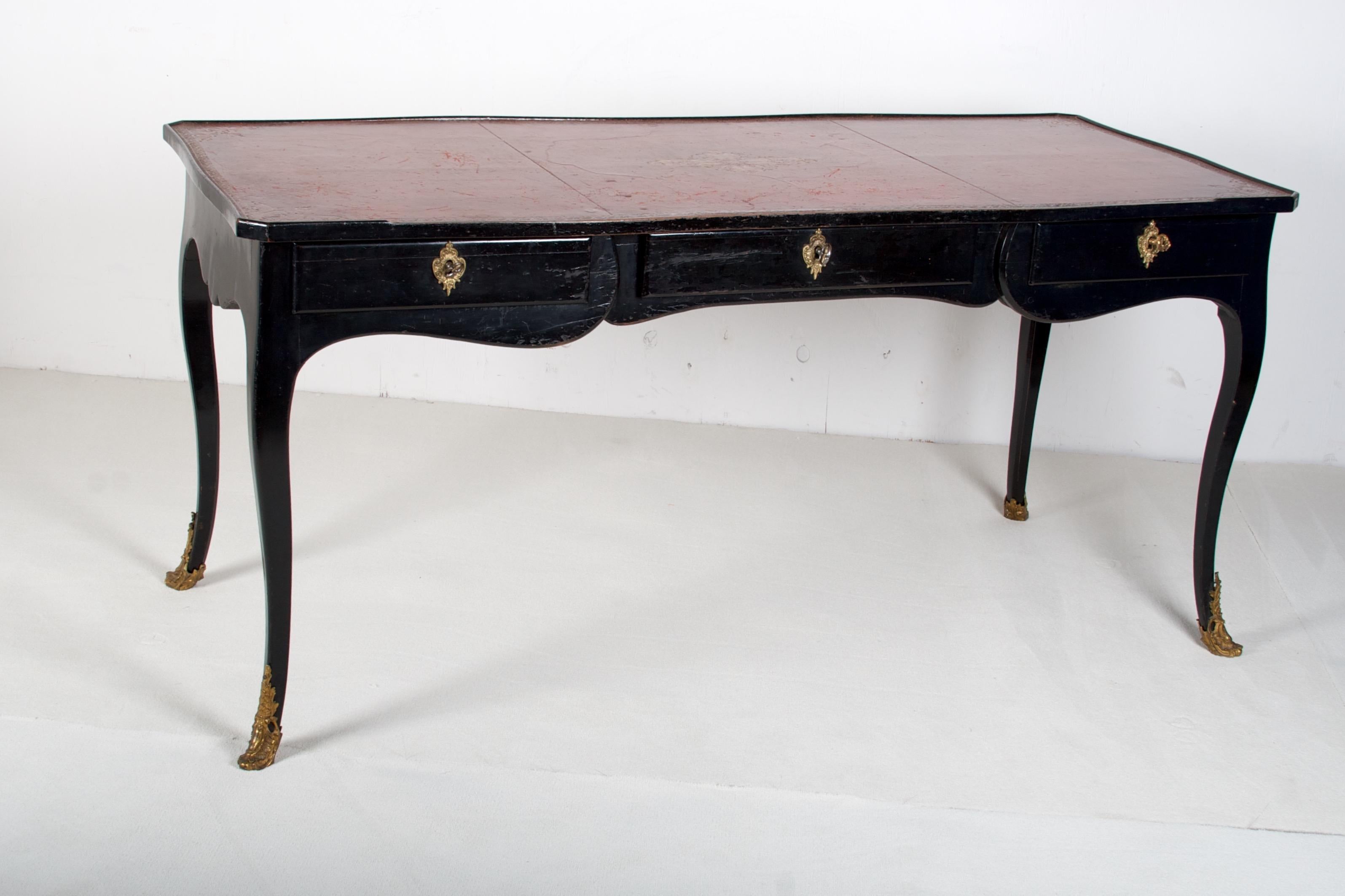 Ebonized shaped rectangular top, inset with raspberry colored gilt tooled leather. Three frieze drawers with brass key plates, opposing dummy drawers, all on cabriolet legs trimmed with
brass sabots.

 