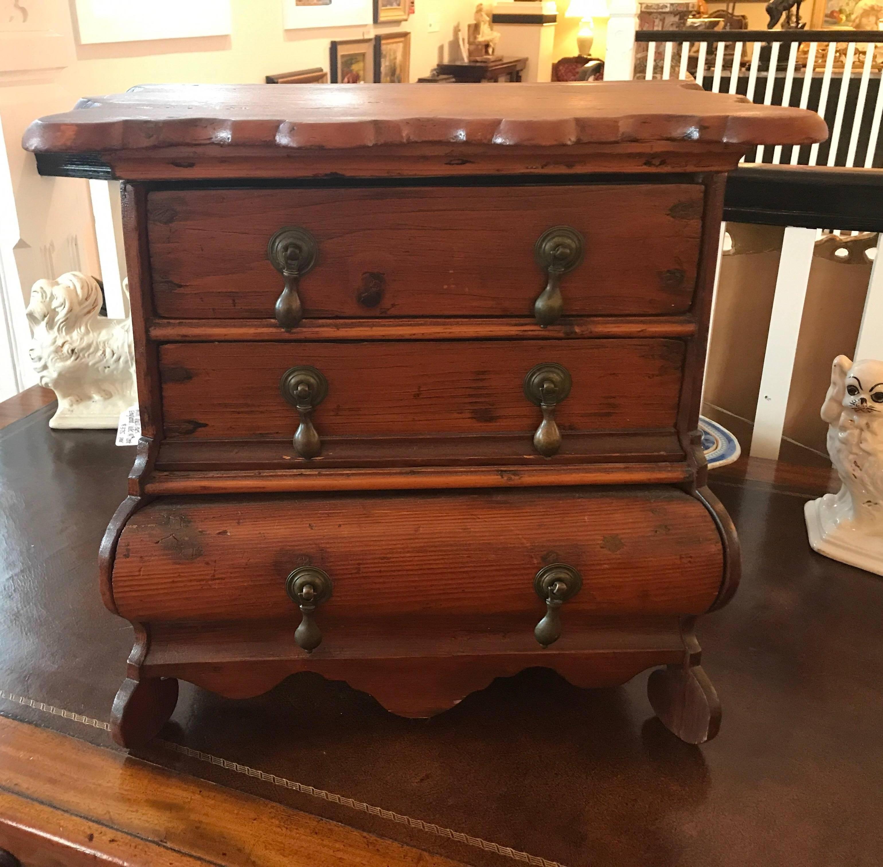 Dutch miniature chest of drawers of detailed pine with boldly scalloped top above a case fitted with three graduated drawers. The Bombay form raised on scalloped feet with a nice aged patina.