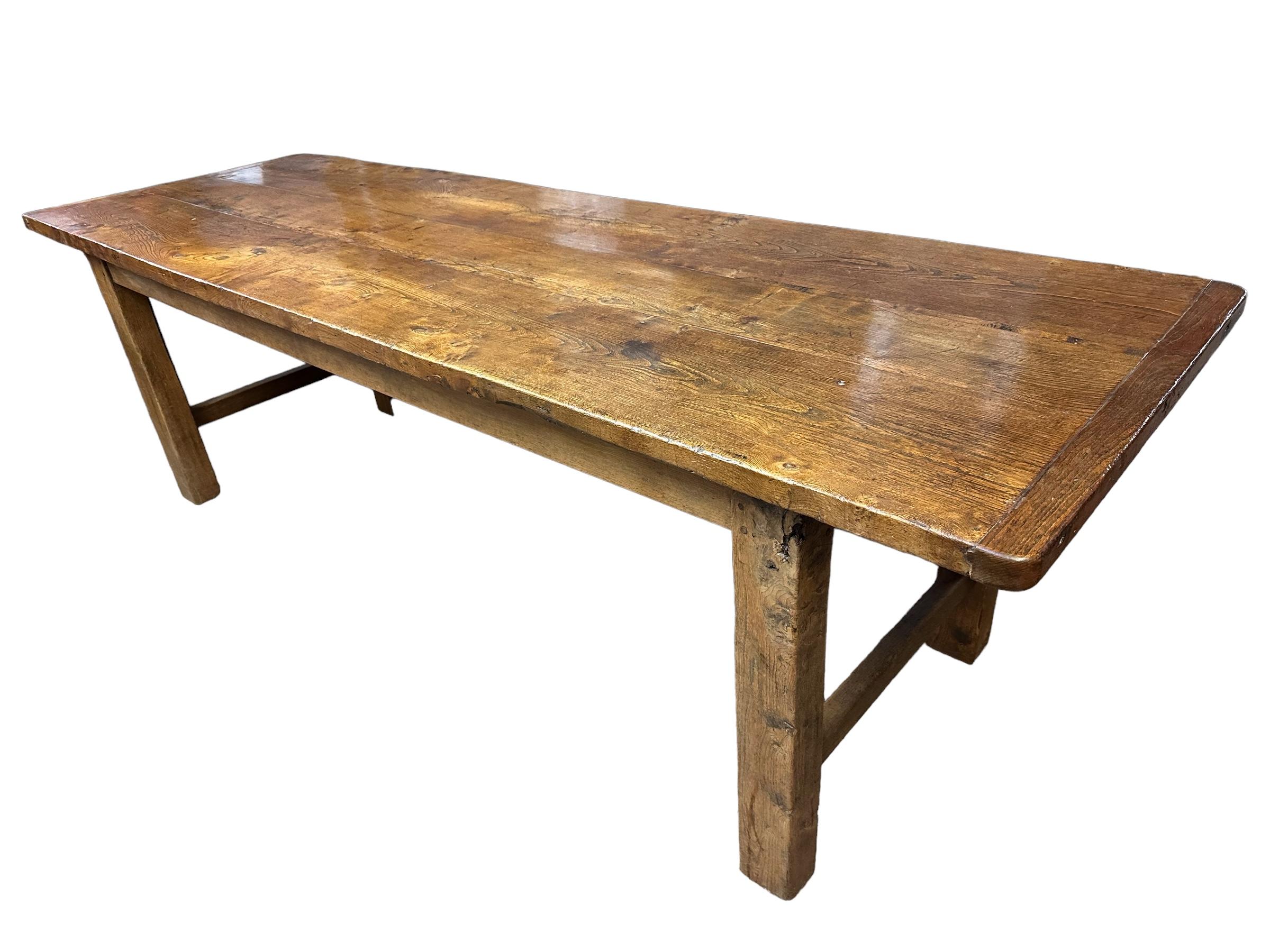 This is a sturdy elm farmhouse table from the early 19th century. It features a strong base with four square legs connected by end stretchers. The has a lovely patina and colour, and the top is full of character with cleated ends. it is a fantastic