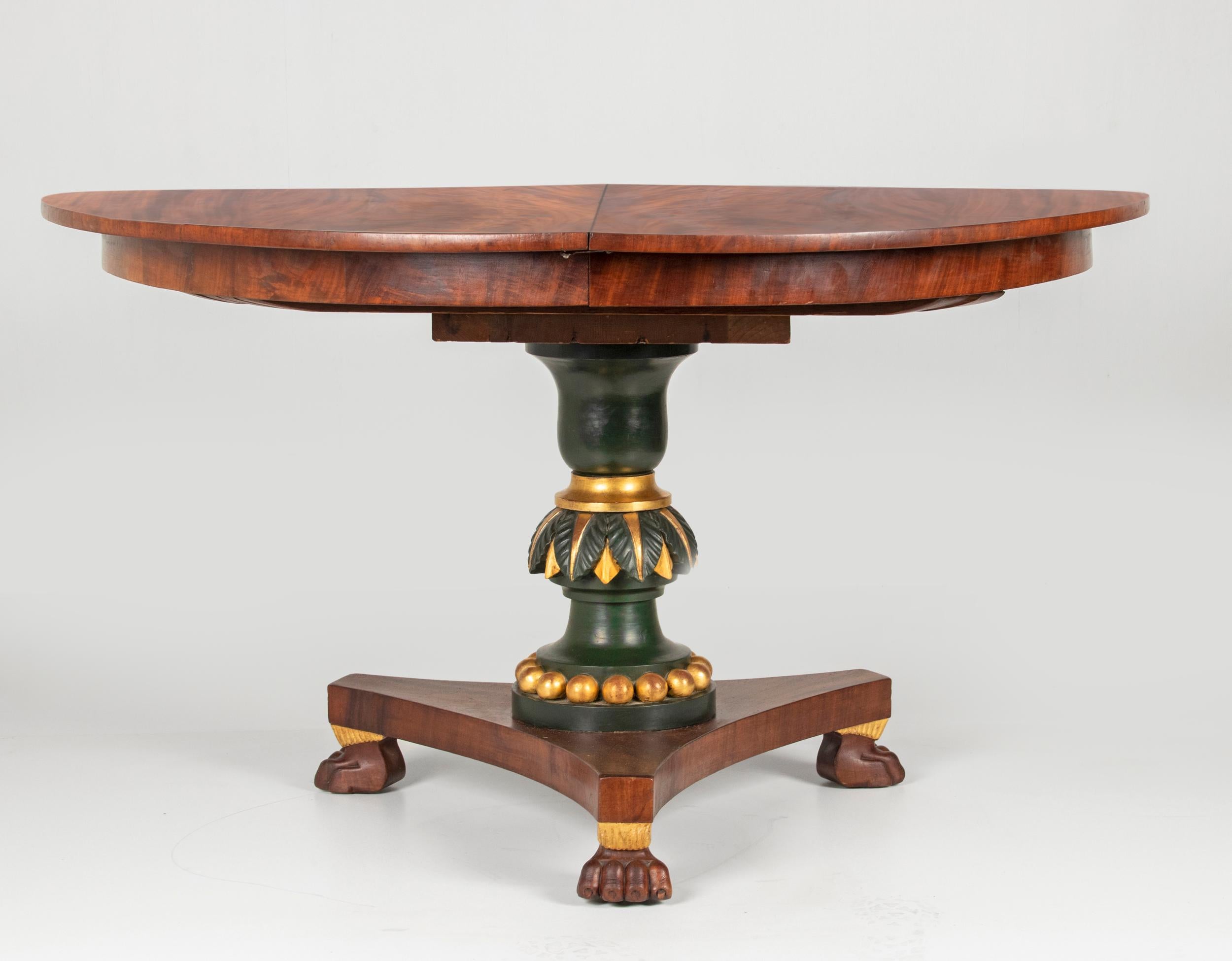An antique Empire period dining room table. This more than 200 years old table is made of mahogany venee. The top rests on a three-legged base, on carved lion-claw legs. The column is dark green patinated with gold leaf accents. This table is also