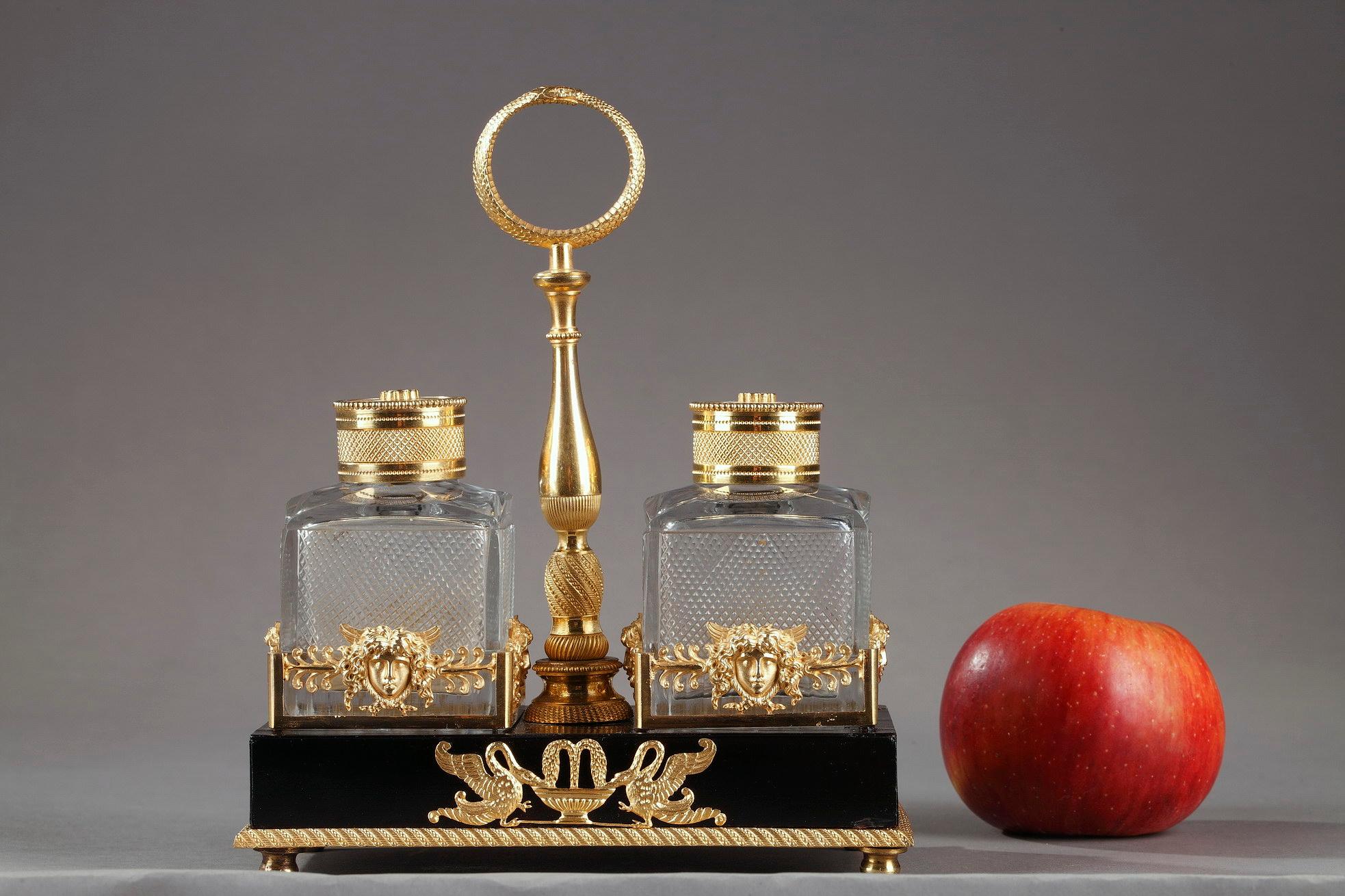 Empire inkstand crafted of ebony, gilt bronze and crystal. Exhibiting an exquisite design of Mercury heads and palmette, this set is comprised of two cut-crystal jars, serving as an inkwell, upon a rectangular ebony base highlighted with swans