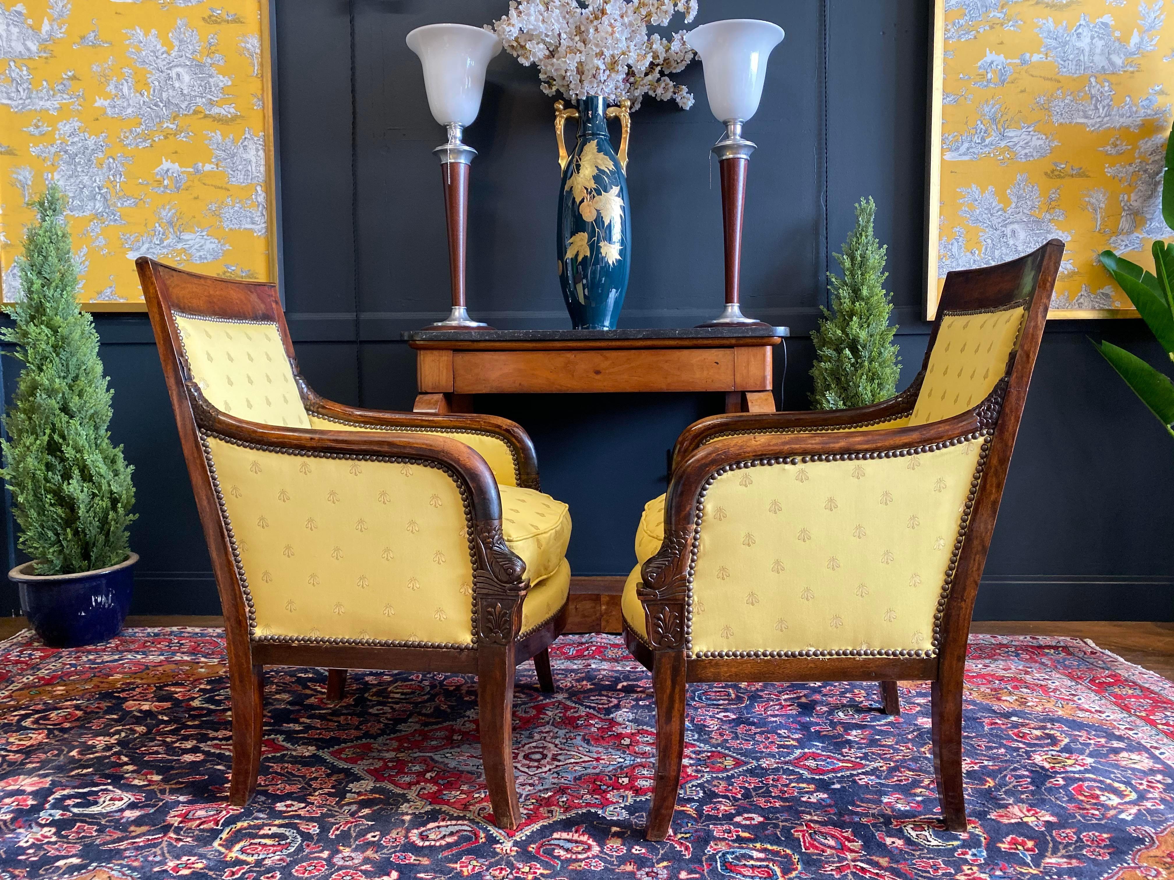 A 1830s pair of Empire mahogany French bergères Aux Dauphins Empire armchairs in the manner of Pierre Bellange (1760-1844). The mahogany frame with sabre front legs continuing as arm supports, the back legs raked. The arms curved and carved with a