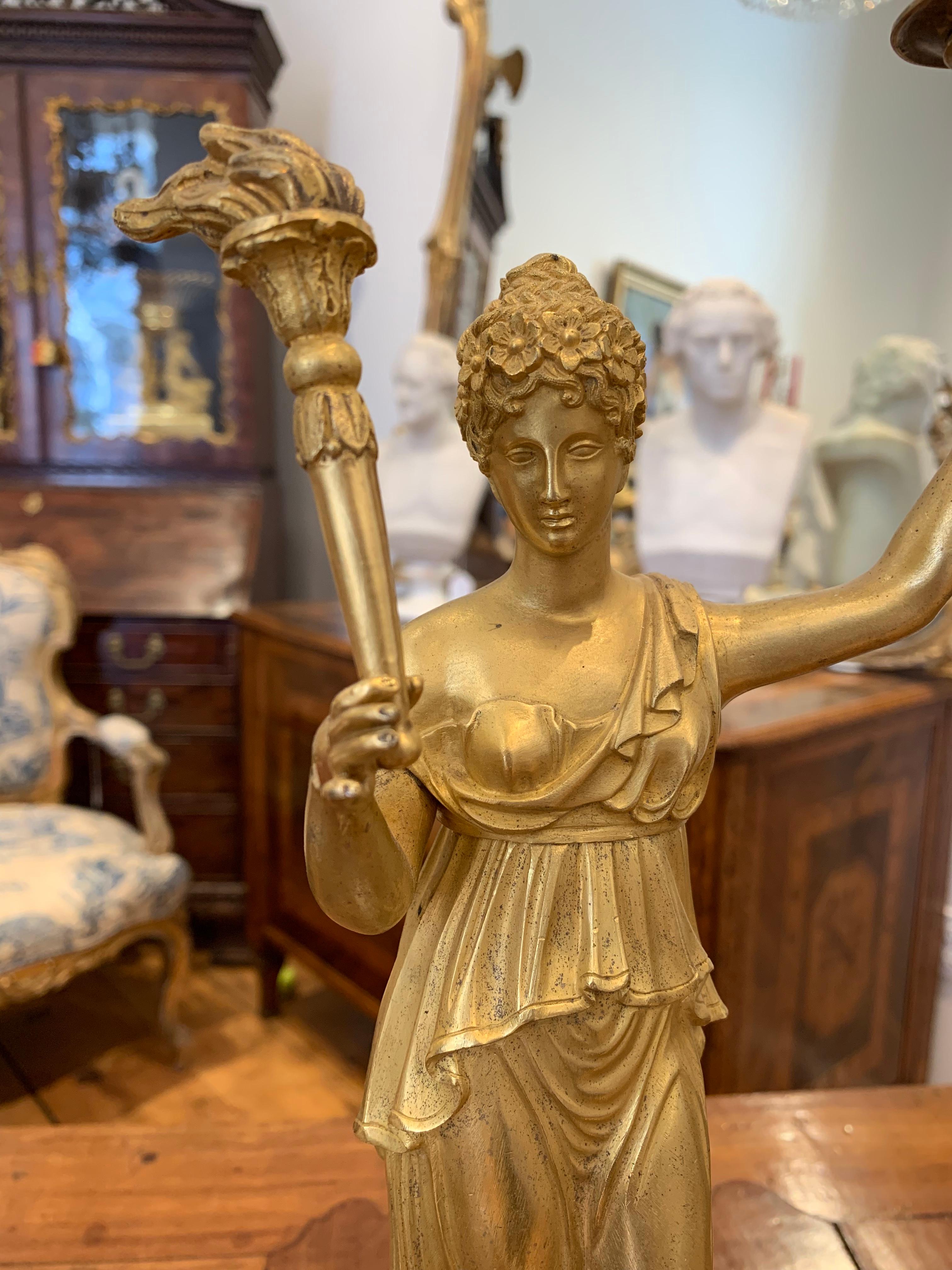 Early 19th century gilt bronze and marble candlestick or candelabrum. Of neoclassical form, a woman holding a torch to light
an urn with candle. Great gold quality.