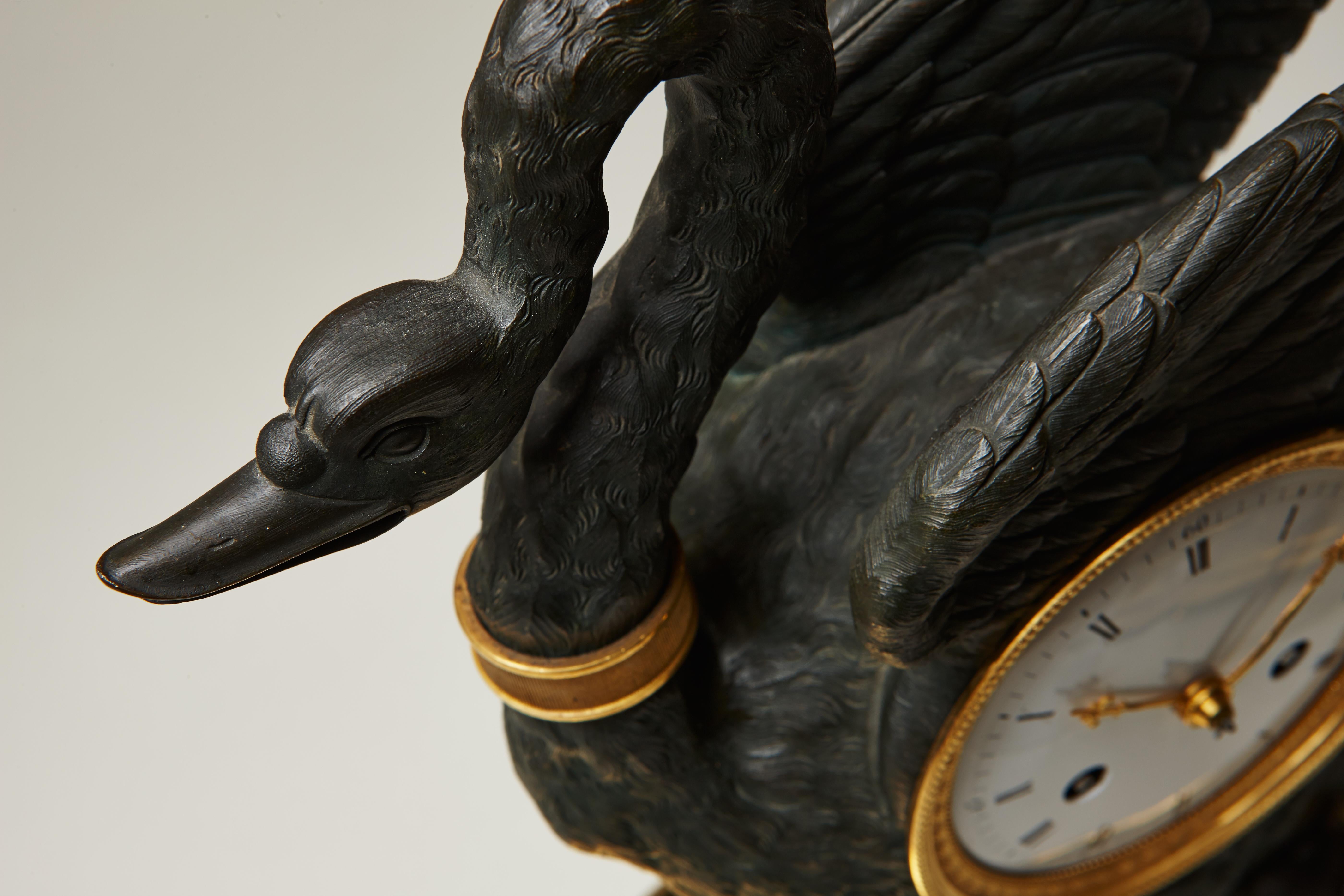 The gilt bronze and patinated figural Napoleonic mantel clock, the drum mounted within a patinated swan, the white enamel dial with Roman hours and Arabic quarters, pierced ormolu hands, the eight-day movement with silk suspended pendulum and