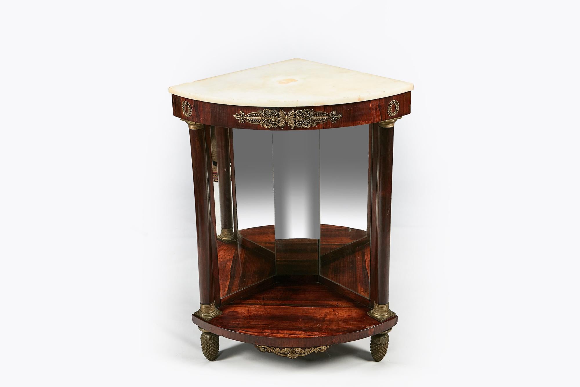 Early 19th century Empire pair of mahogany marble topped corner console tables, the statuary marble top supported by bowfront apron with centred medallion ormolu filigree flanked with ormolu laurel wreath mounts raised over mirrored panel flanked