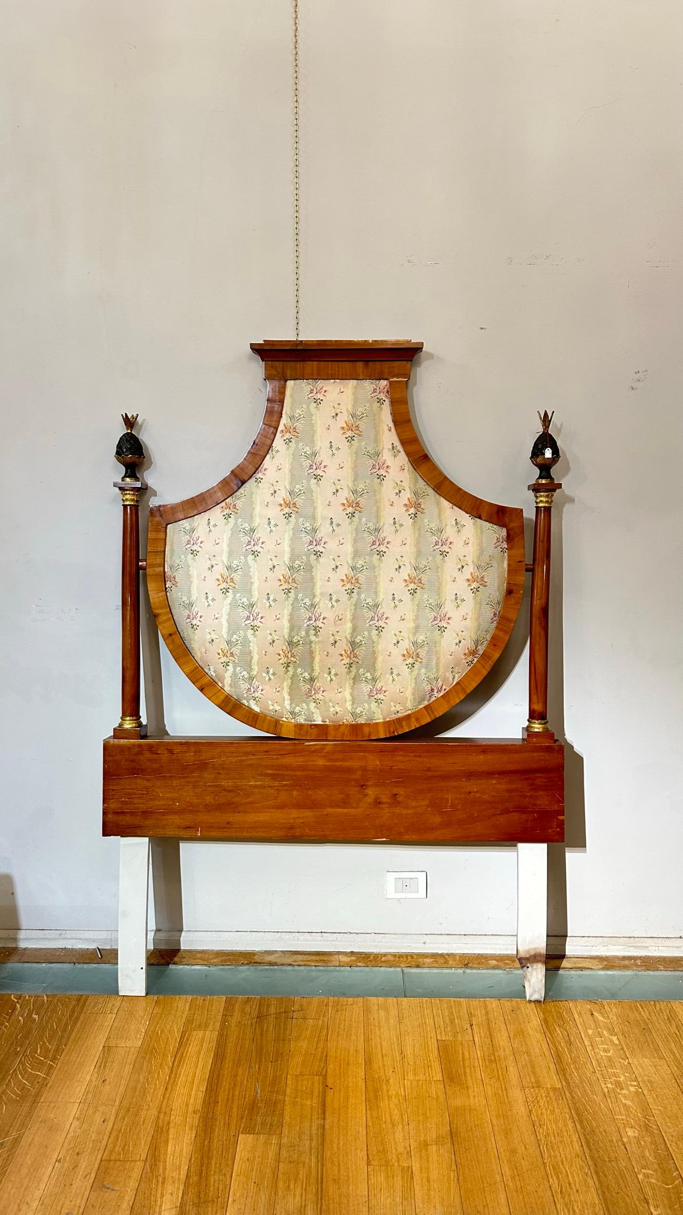 This beautiful Empire period shield headboard, dating to around 1810, is a masterpiece of craftsmanship made entirely of cherry wood. The gilded and carved wood finishes give a touch of elegance and refinement to its design. The headboard has been
